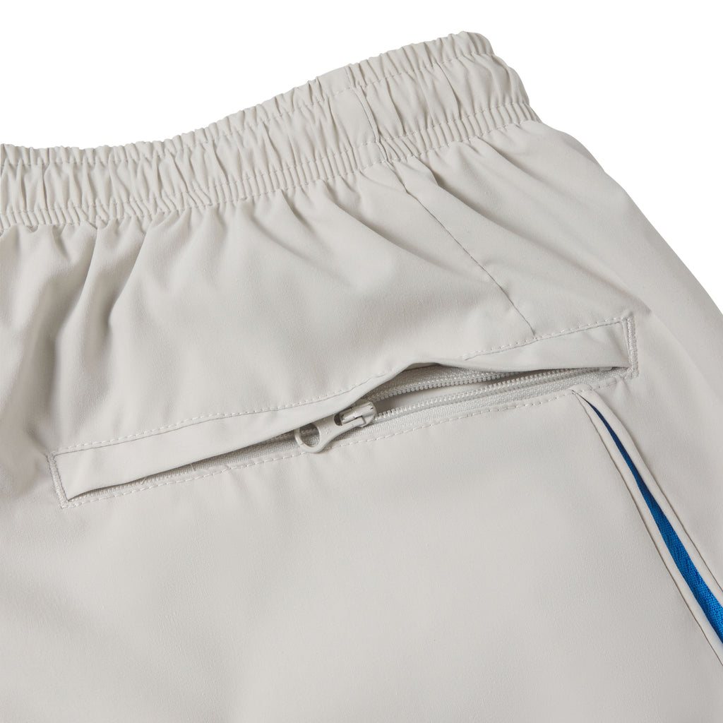 Beige nylon track pant with an elastic waistband, zippered side pocket, and blue contrast side panel detailing.