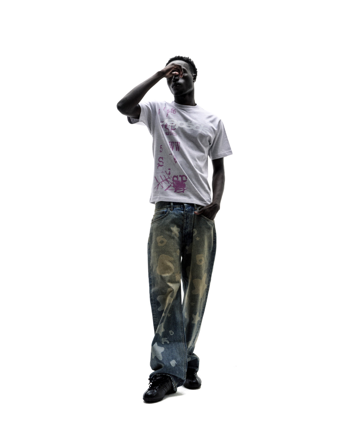 A model wearing a grey graphic t-shirt and baggy, star-patterned denim jeans, posing against a white background.