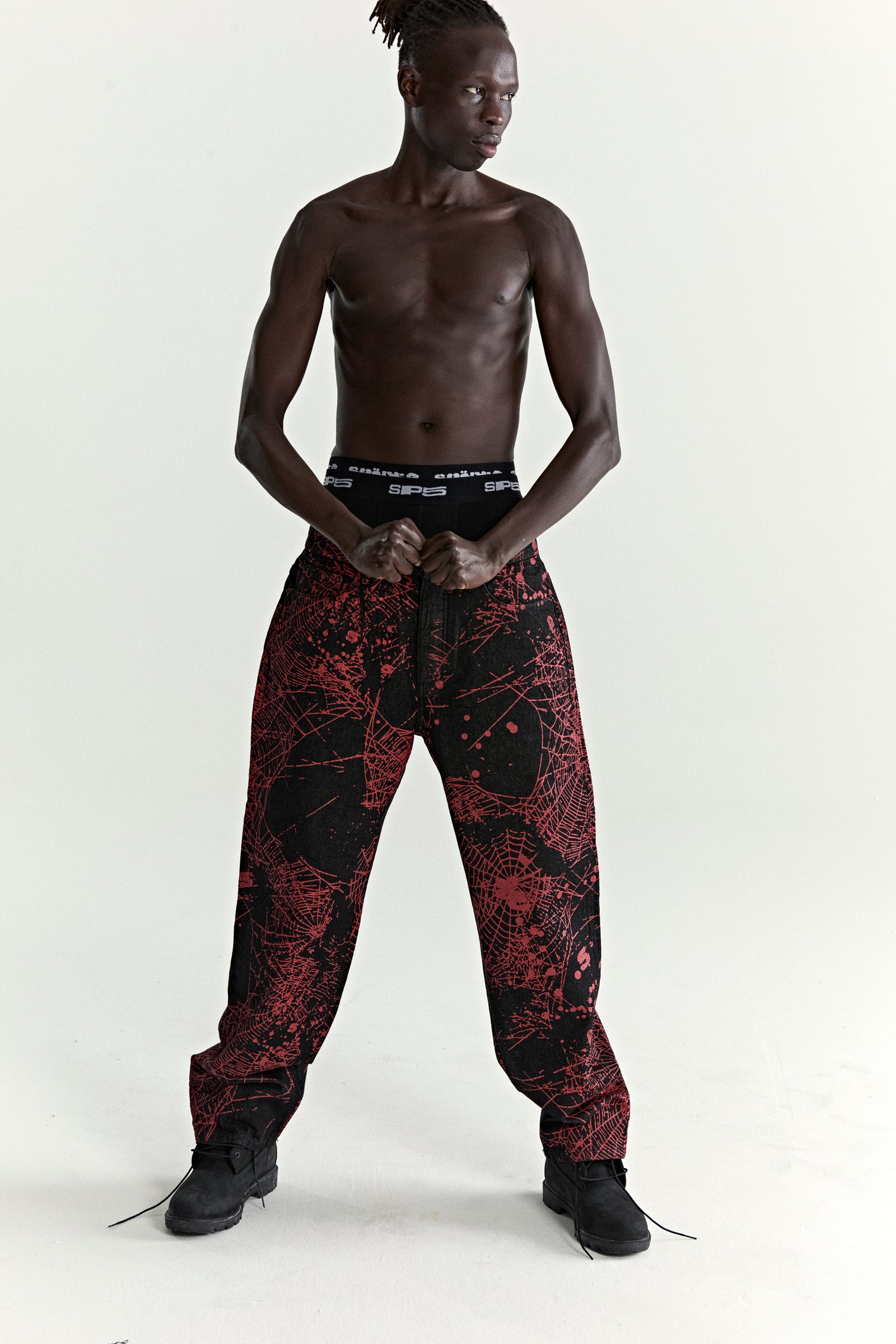 Black denim pants with all-over red web print, classic straight leg fit, and branded hardware.