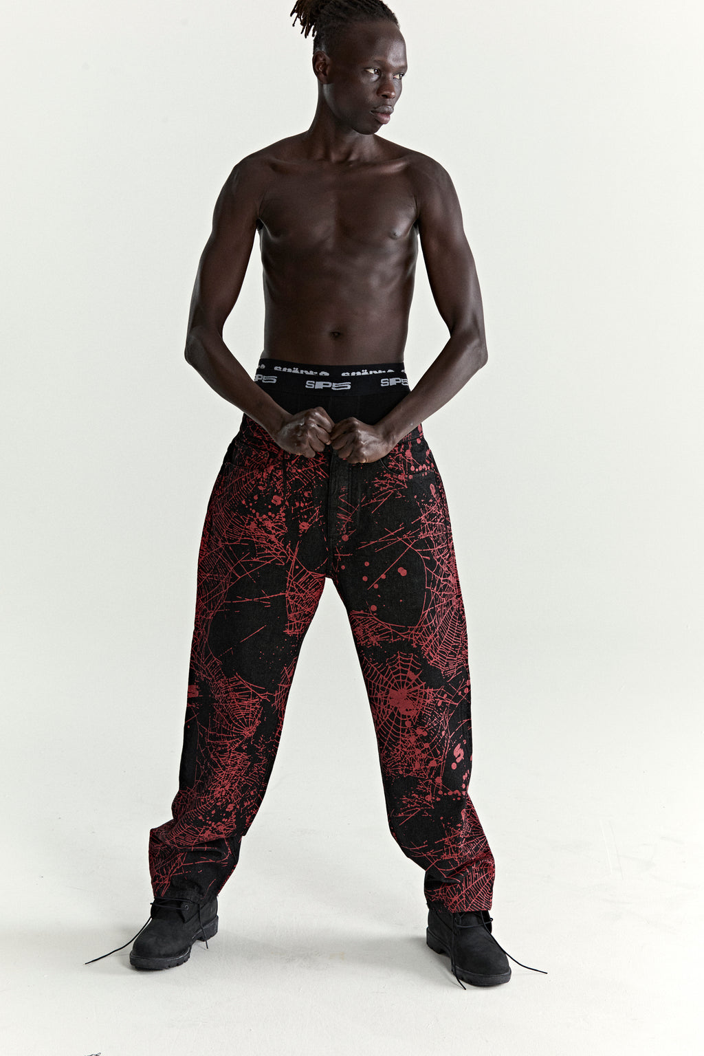 Black denim pants with all-over red web print, classic straight leg fit, and branded hardware.