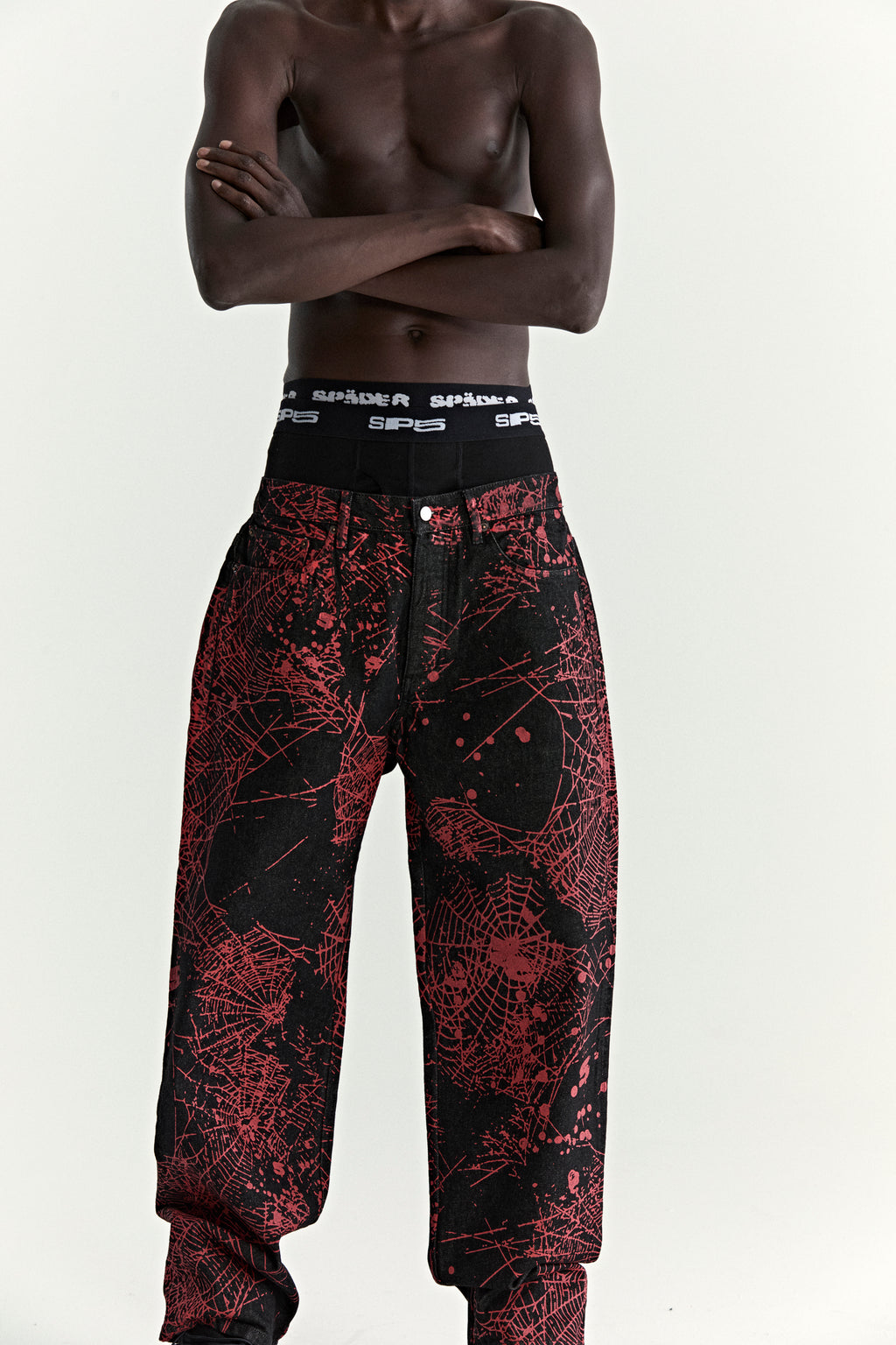 Black denim pants with all-over red web print, five-pocket styling, and a straight leg fit.