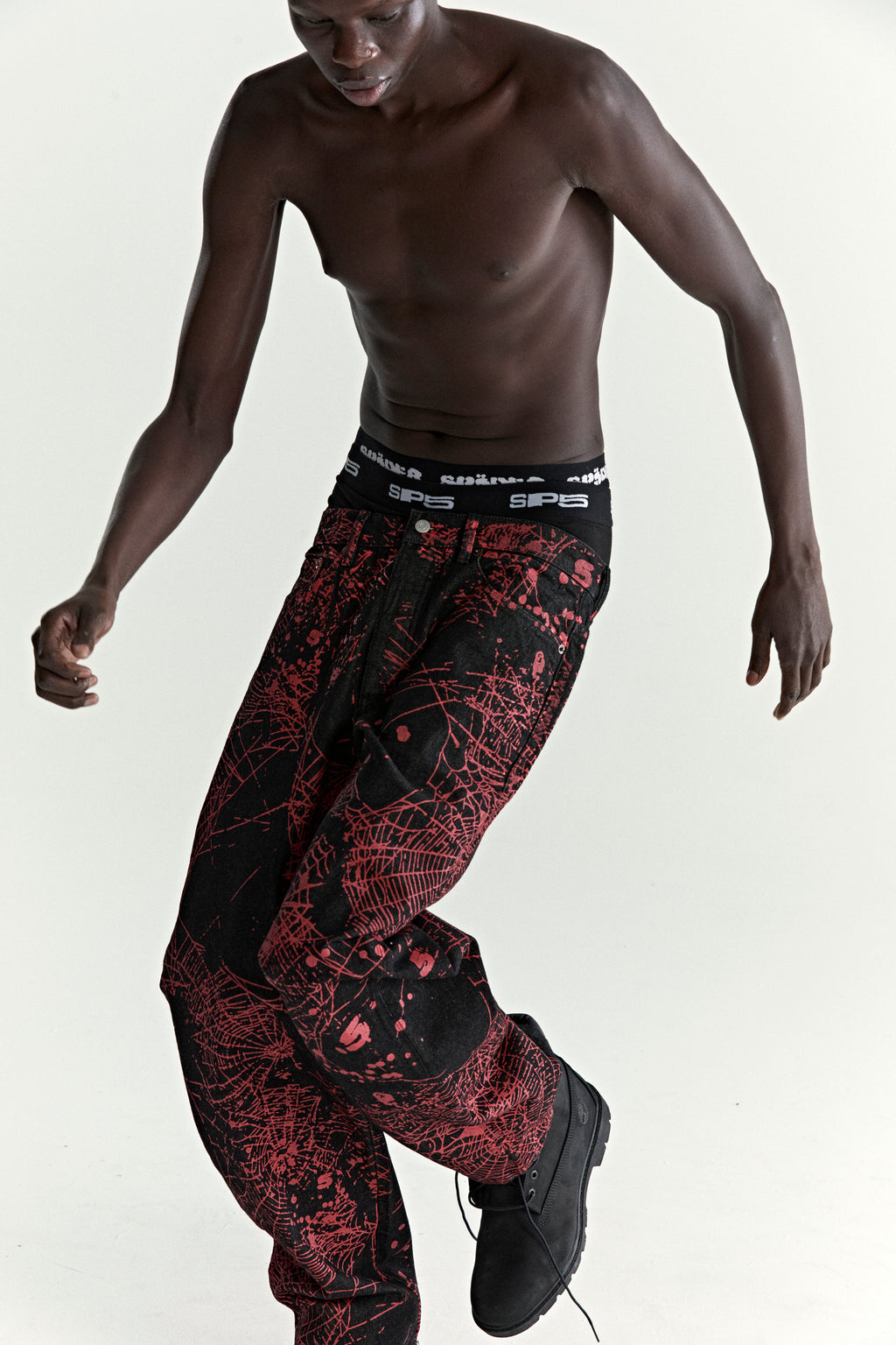 Black denim pants with red all-over web print, classic straight leg fit, and SP5DER branding.
