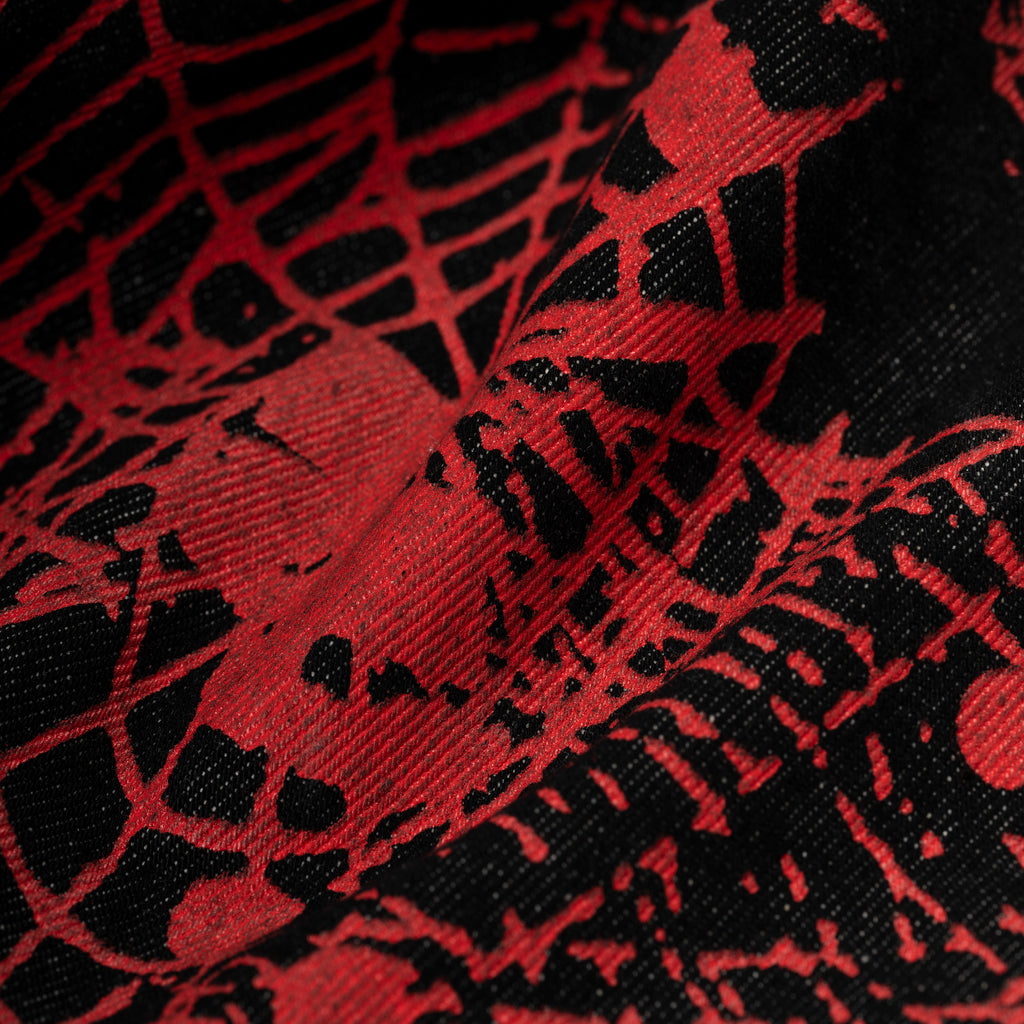 Close-up of V2 WEB DENIM fabric, showing black denim with a bold red all-over web print design.