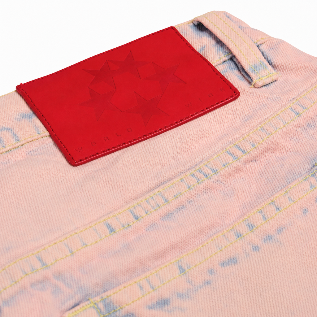 Light pink acid-wash denim jeans featuring a bold red branded leather patch with embossed star graphic design.