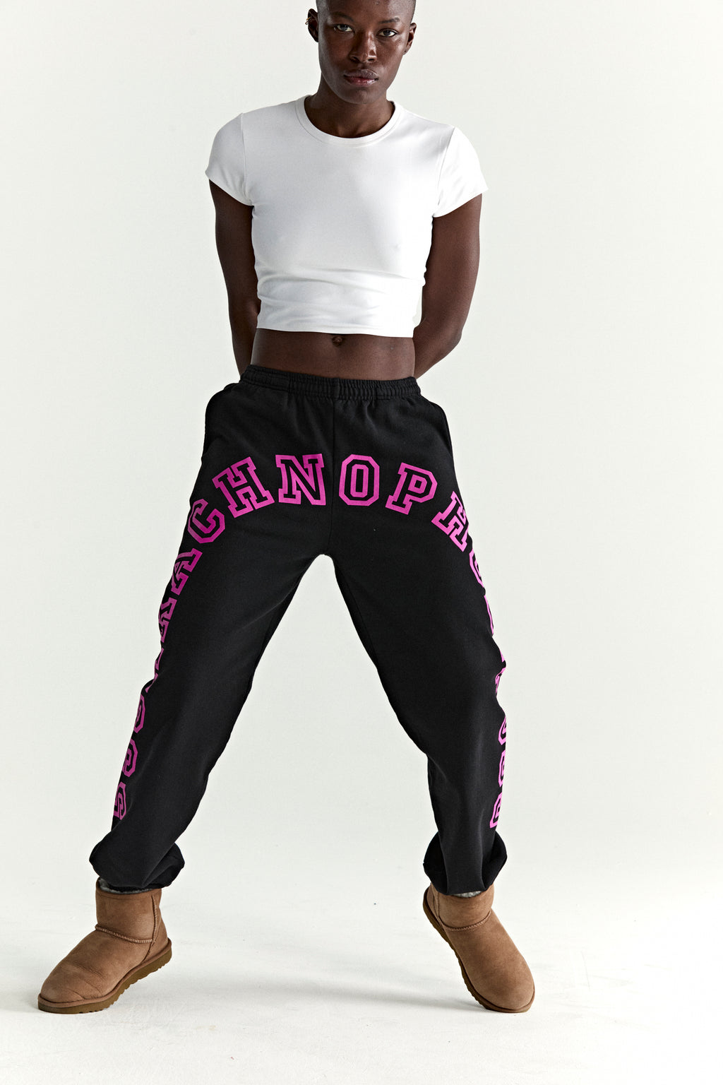 Black ARACH SWEATPANTS with arched pink puff print text, elasticized waistband, and cuffs, worn by a model.