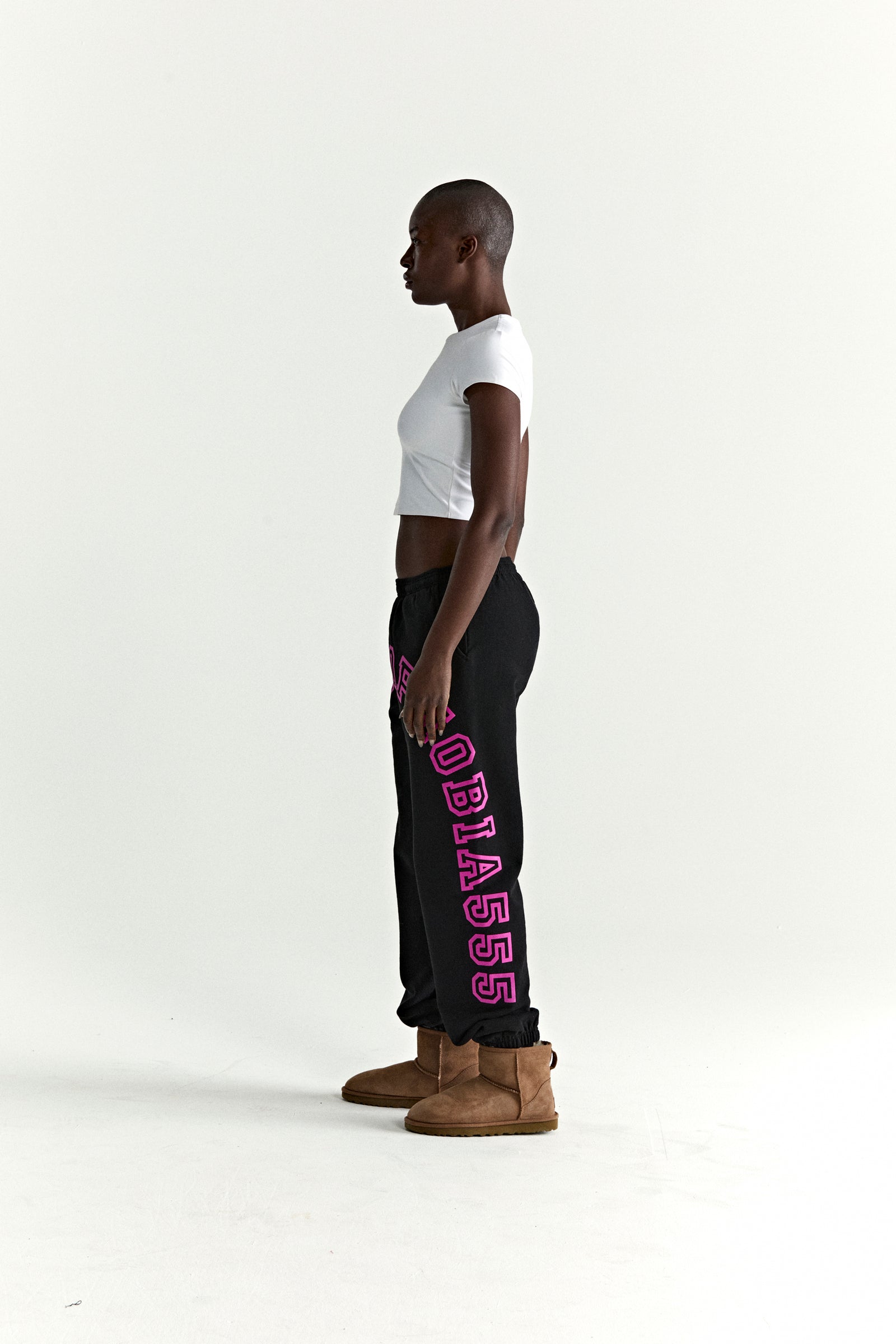 Black cotton fleece sweatpants with arched pink text print, worn by a model in profile.