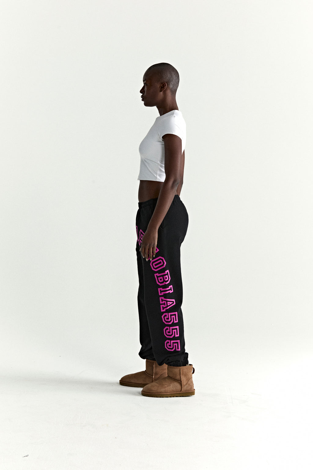 Black cotton fleece sweatpants with arched pink text print, worn by a model in profile.