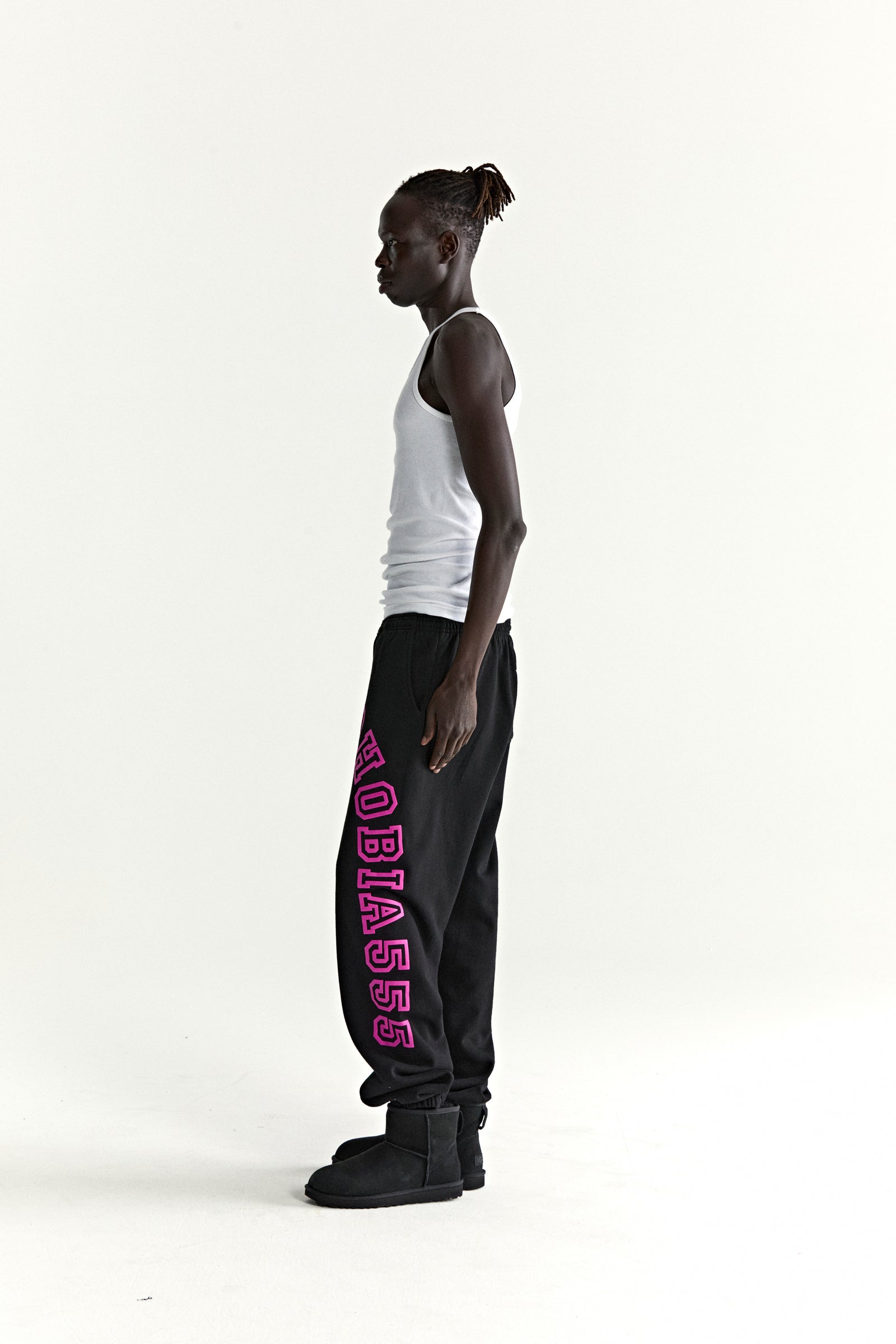 Black ARACH SWEATPANT with pink arched text print, worn by a man in profile.