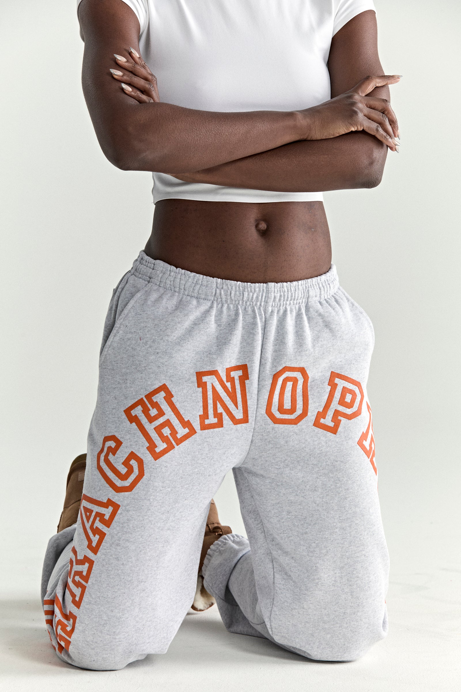 Gray 13oz cotton fleece sweatpants with orange arched text puff print, elastic waistband, and cuffs.