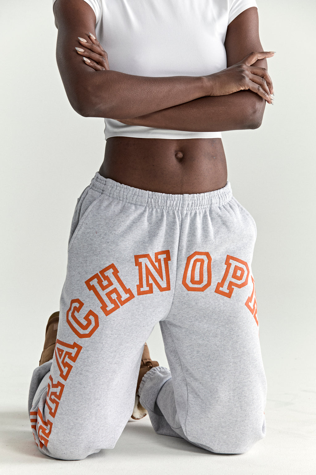 Gray 13oz cotton fleece sweatpants with orange arched text puff print, elastic waistband, and cuffs.