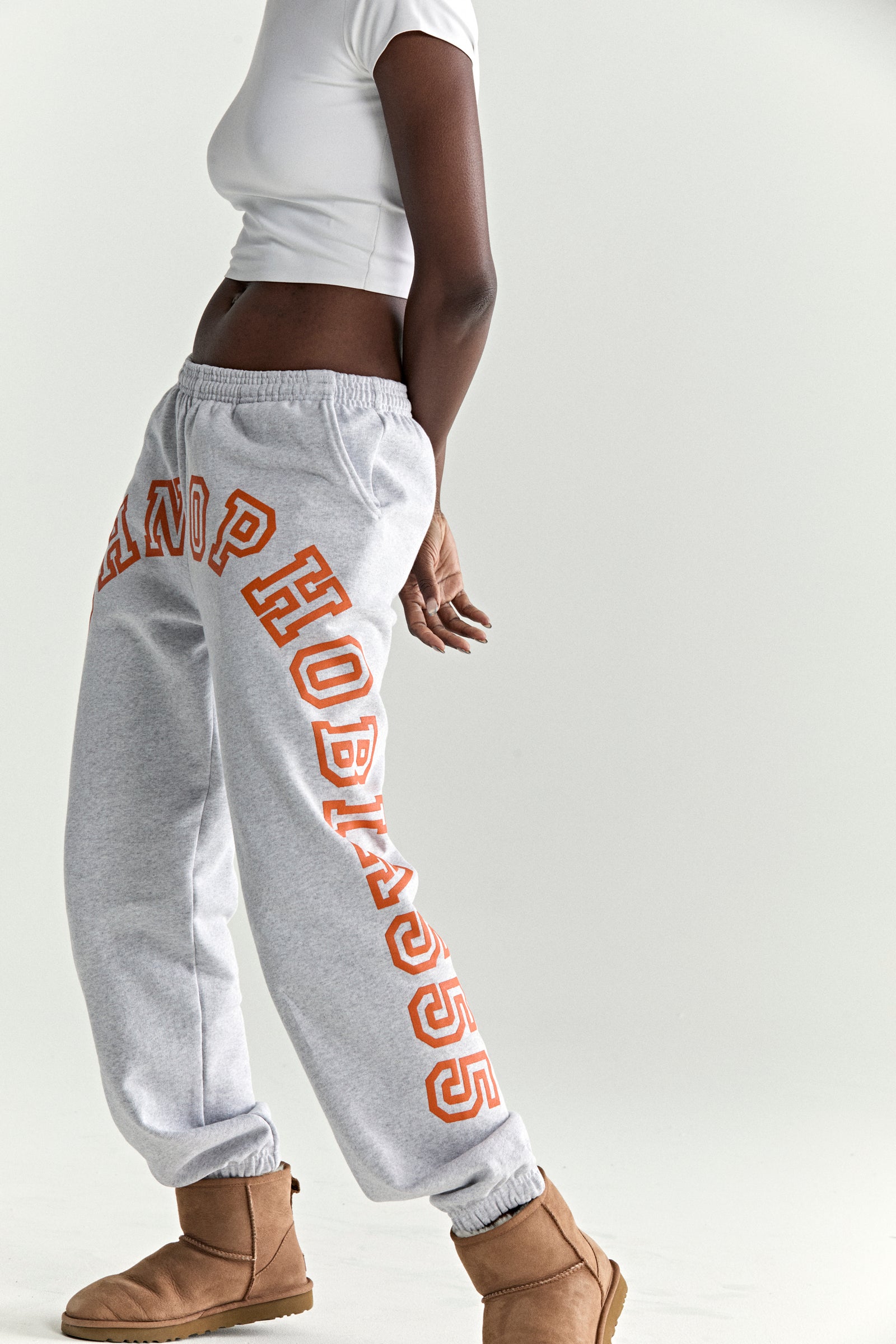 Light grey cotton fleece sweatpants with orange arched text print, elasticized waistband and cuffs.
