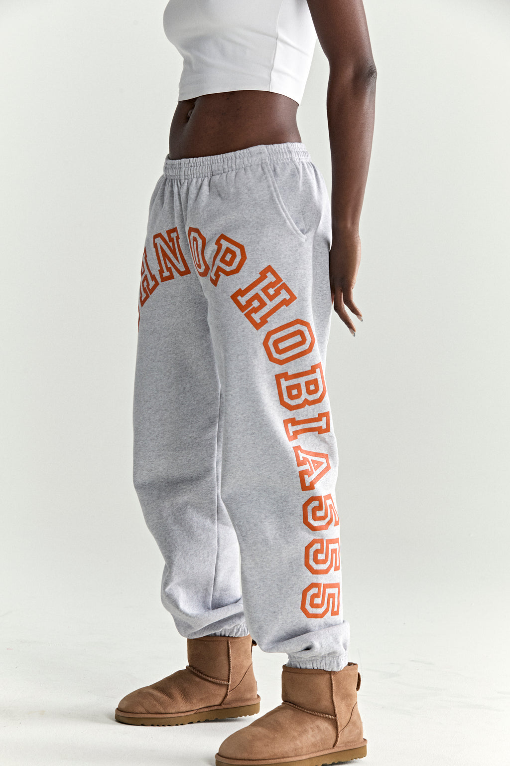 Gray cotton fleece sweatpants with orange arched text print, elasticized waistband and cuffs.