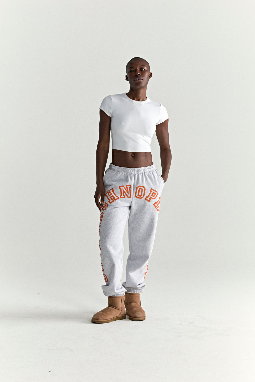 Light grey cotton fleece sweatpants with orange arched text print, elasticized waistband and cuffs.