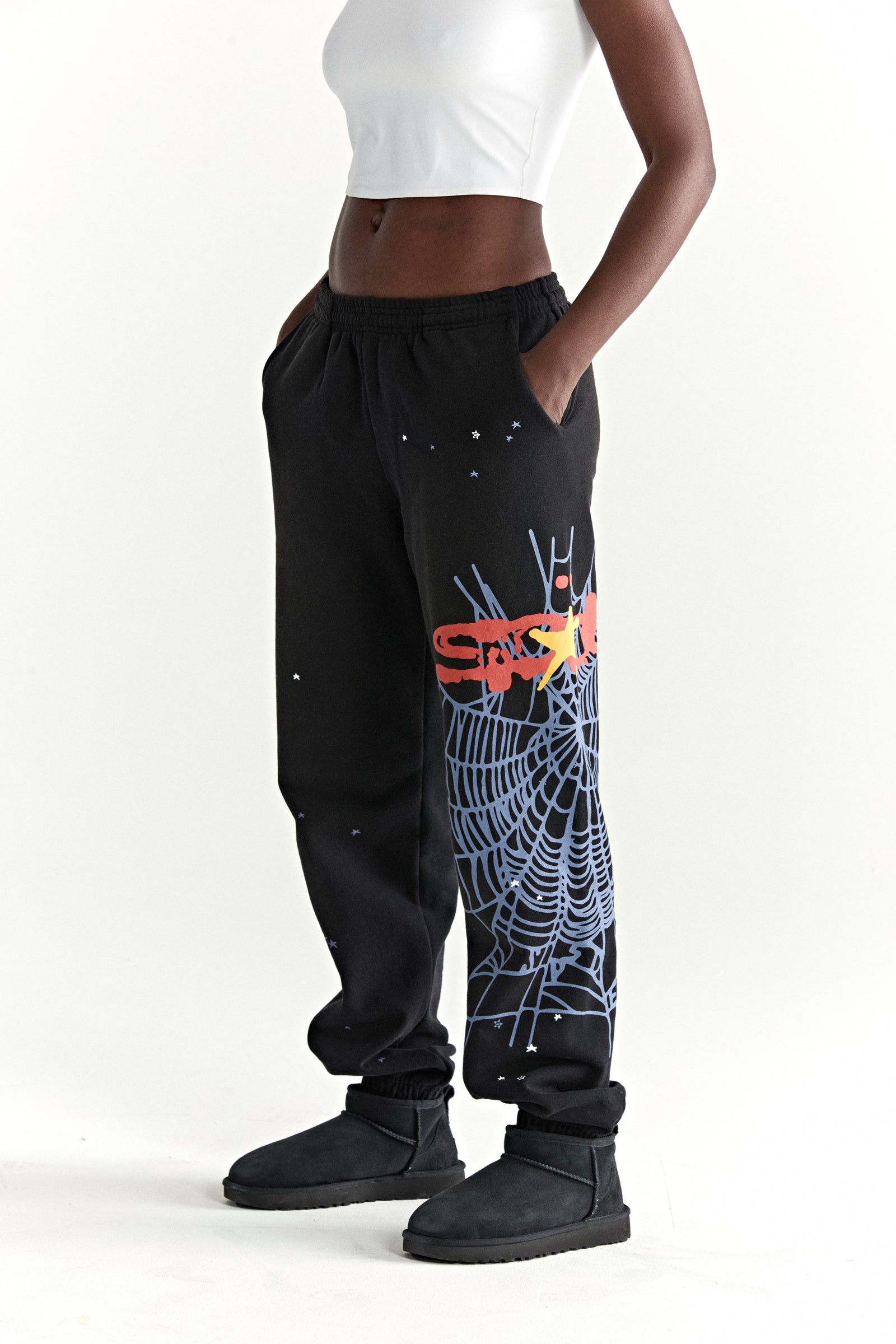 Black 13oz cotton fleece sweatpants with SP5DER web graphic, scattered stars, drawstring waist, and elastic cuffs.