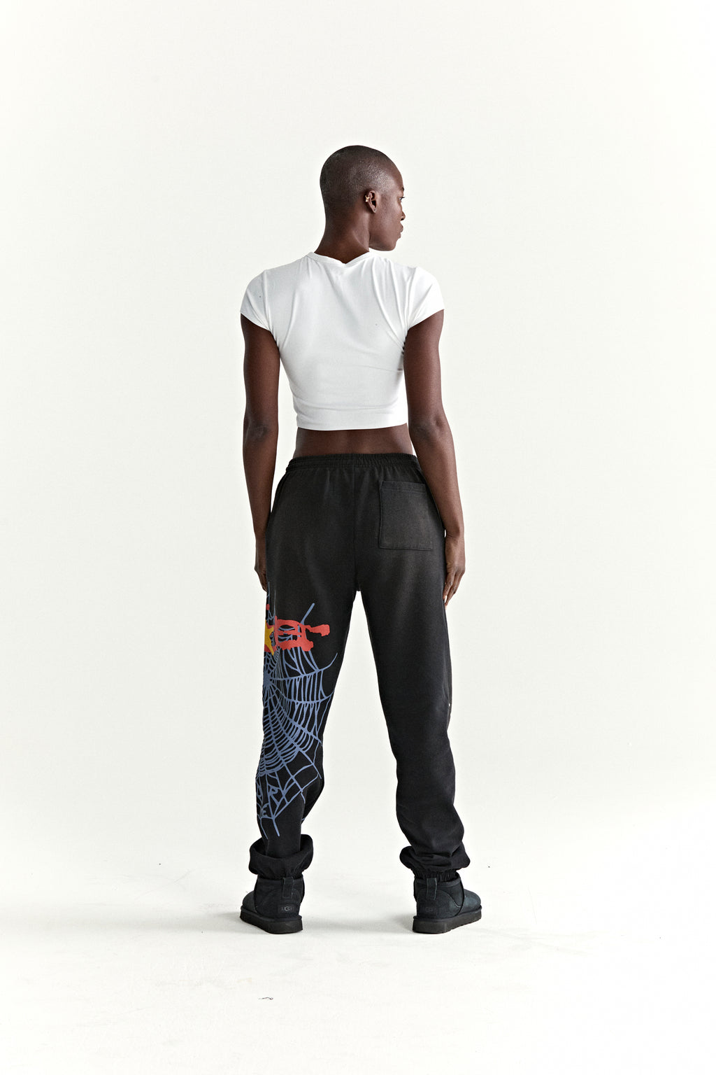 Black HEAVY WEB SWEATPANTS with SP5DER web graphic and scattered stars, worn by a person facing away.