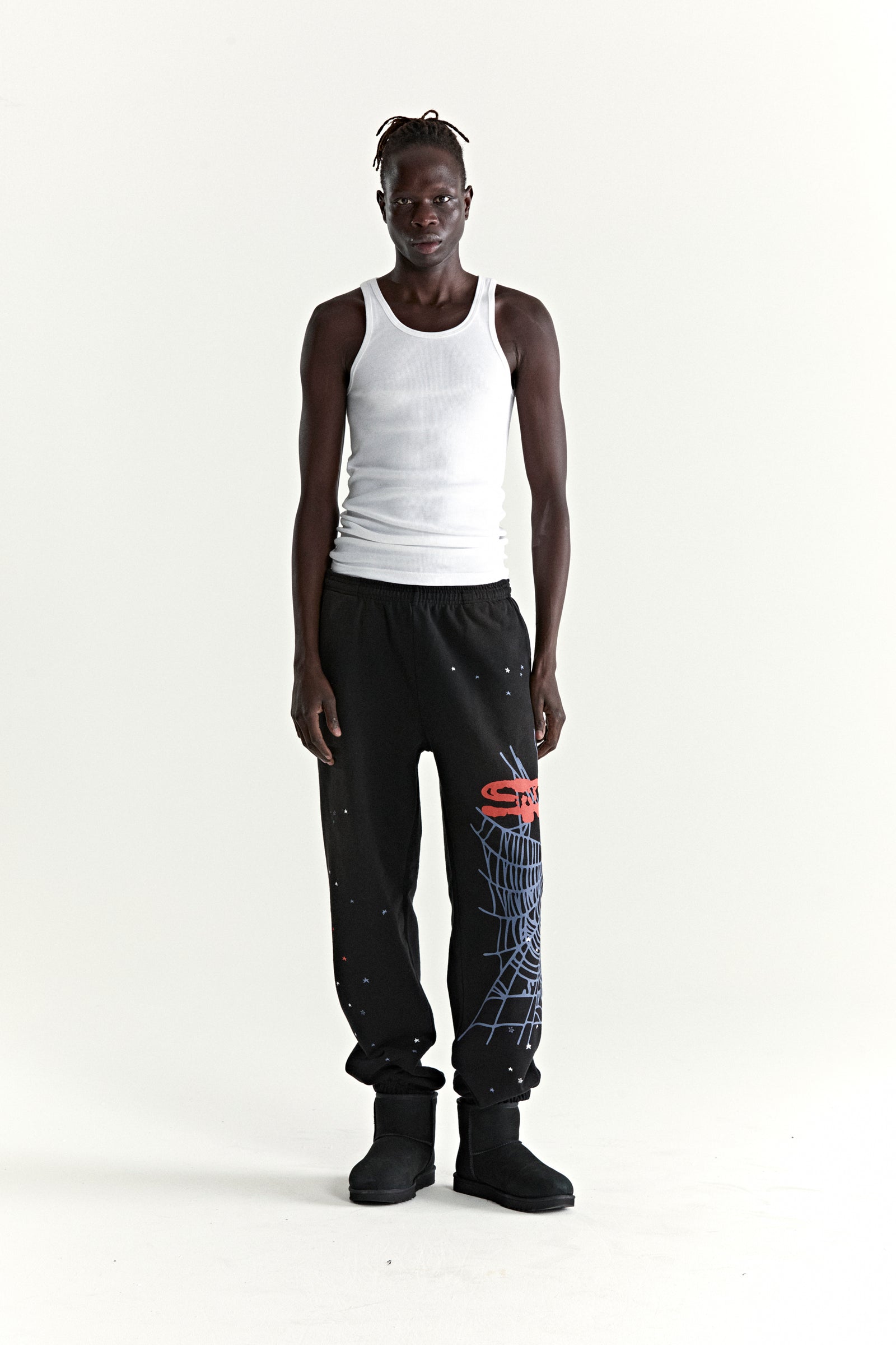 Black HEAVY WEB SWEATPANT with red SP5DER graphic, blue web, and scattered stars, worn by a model.