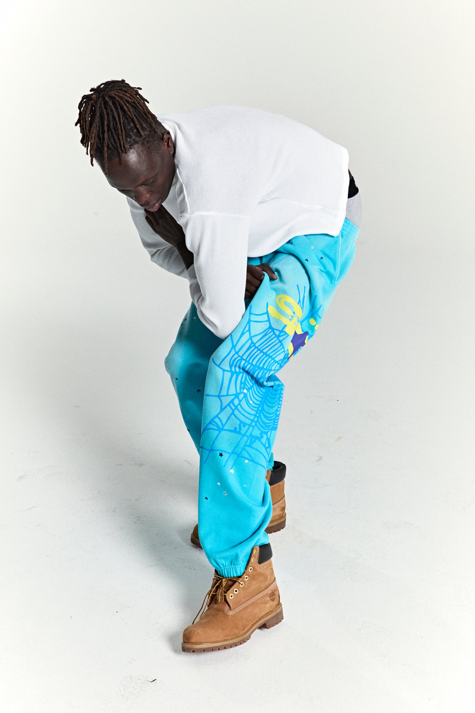 Man wearing blue HEAVY WEB SWEATPANTS with SP5DER web graphic, scattered stars, and elasticized cuffs.