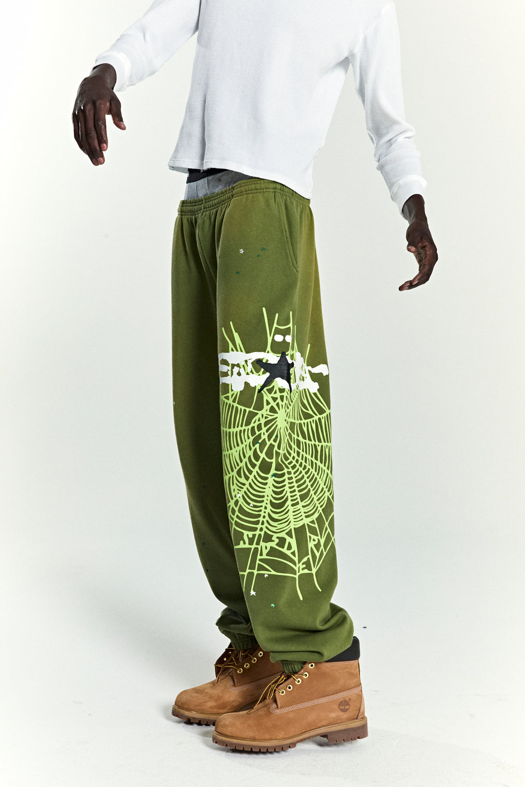 Olive green HEAVY WEB SWEATPANTS with a neon green SP5DER web graphic and scattered stars.