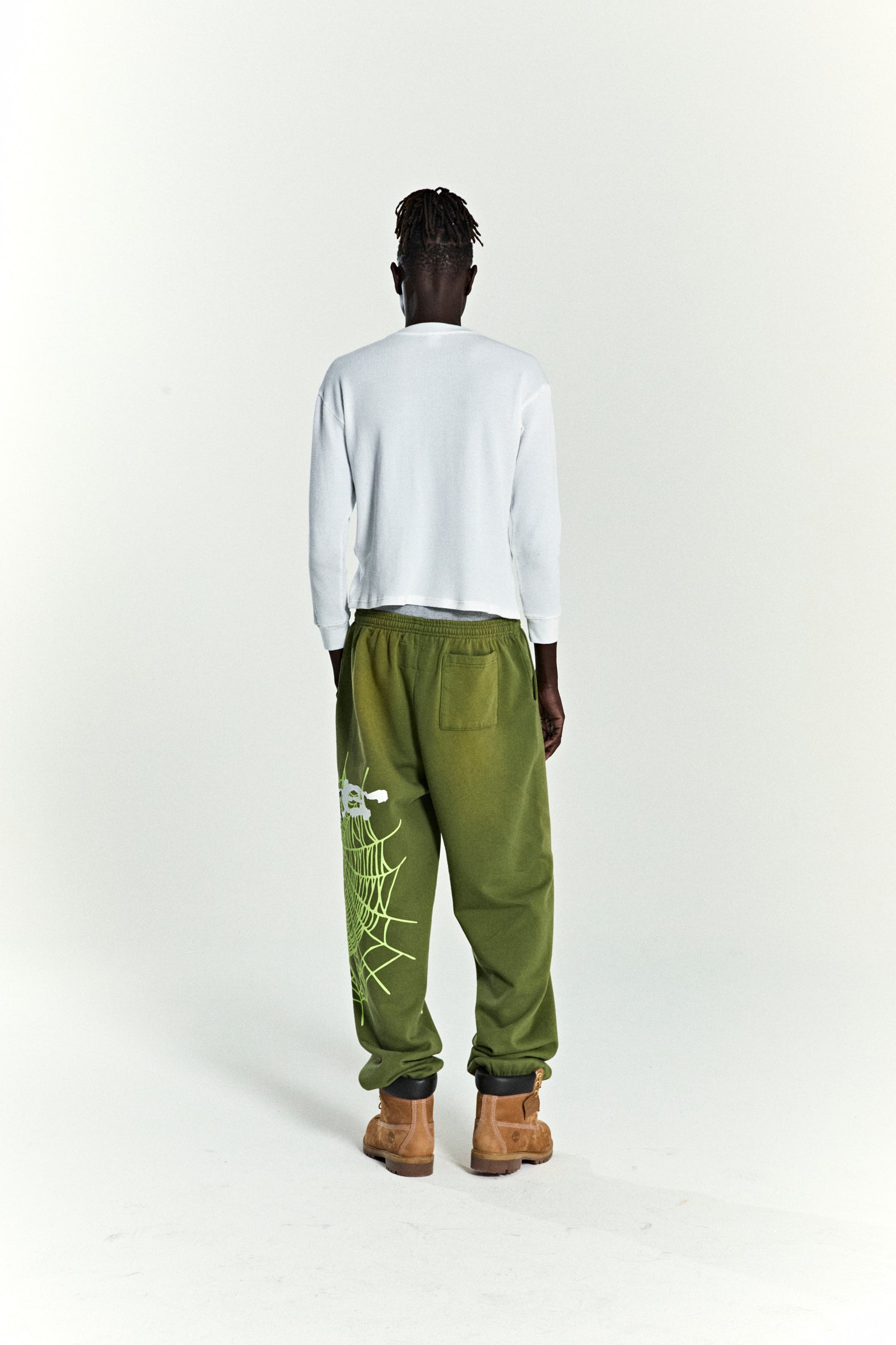Olive green HEAVY WEB SWEATPANT with SP5DER web graphic and scattered stars, worn by a person from behind.