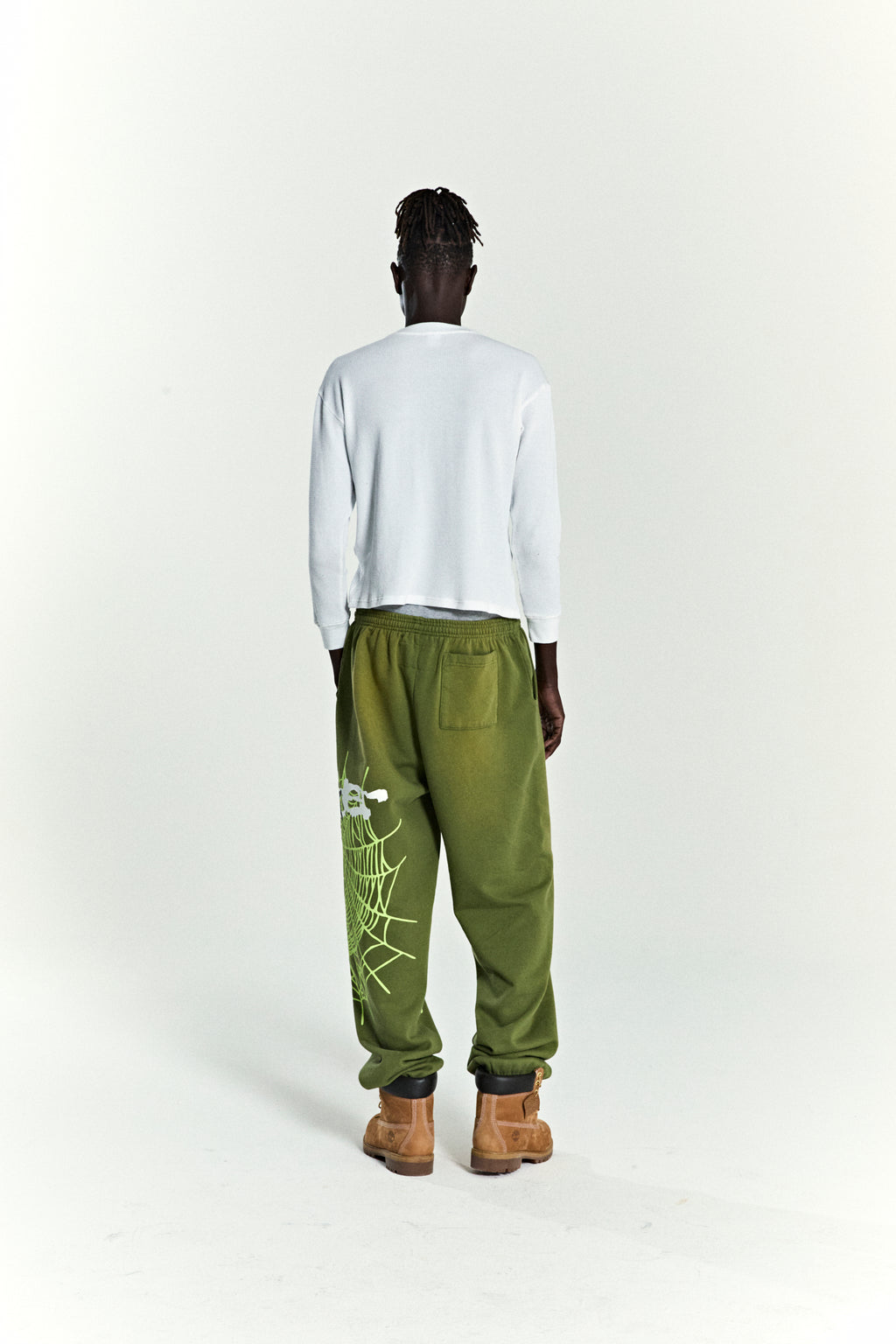 Olive green HEAVY WEB SWEATPANT with SP5DER web graphic and scattered stars, worn by a person from behind.