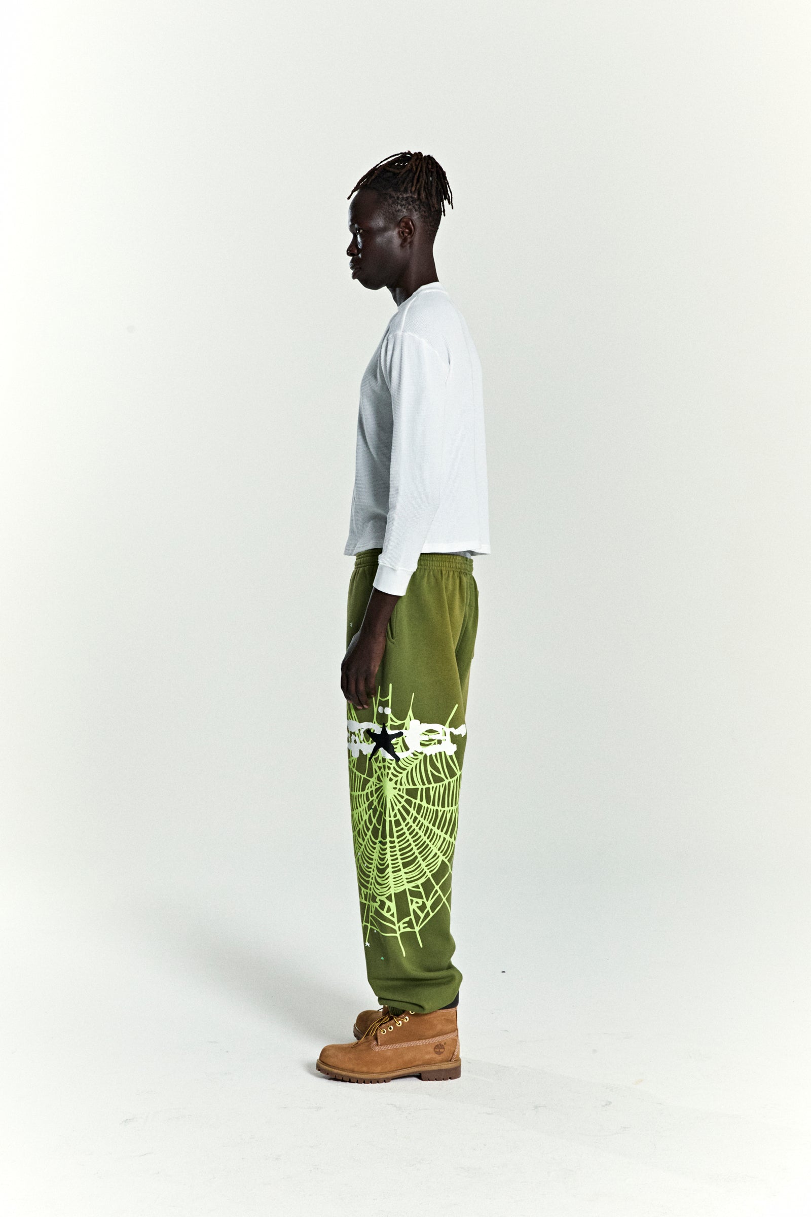 Olive green HEAVY WEB SWEATPANT with white SP5DER web graphic and scattered stars, worn by a model.