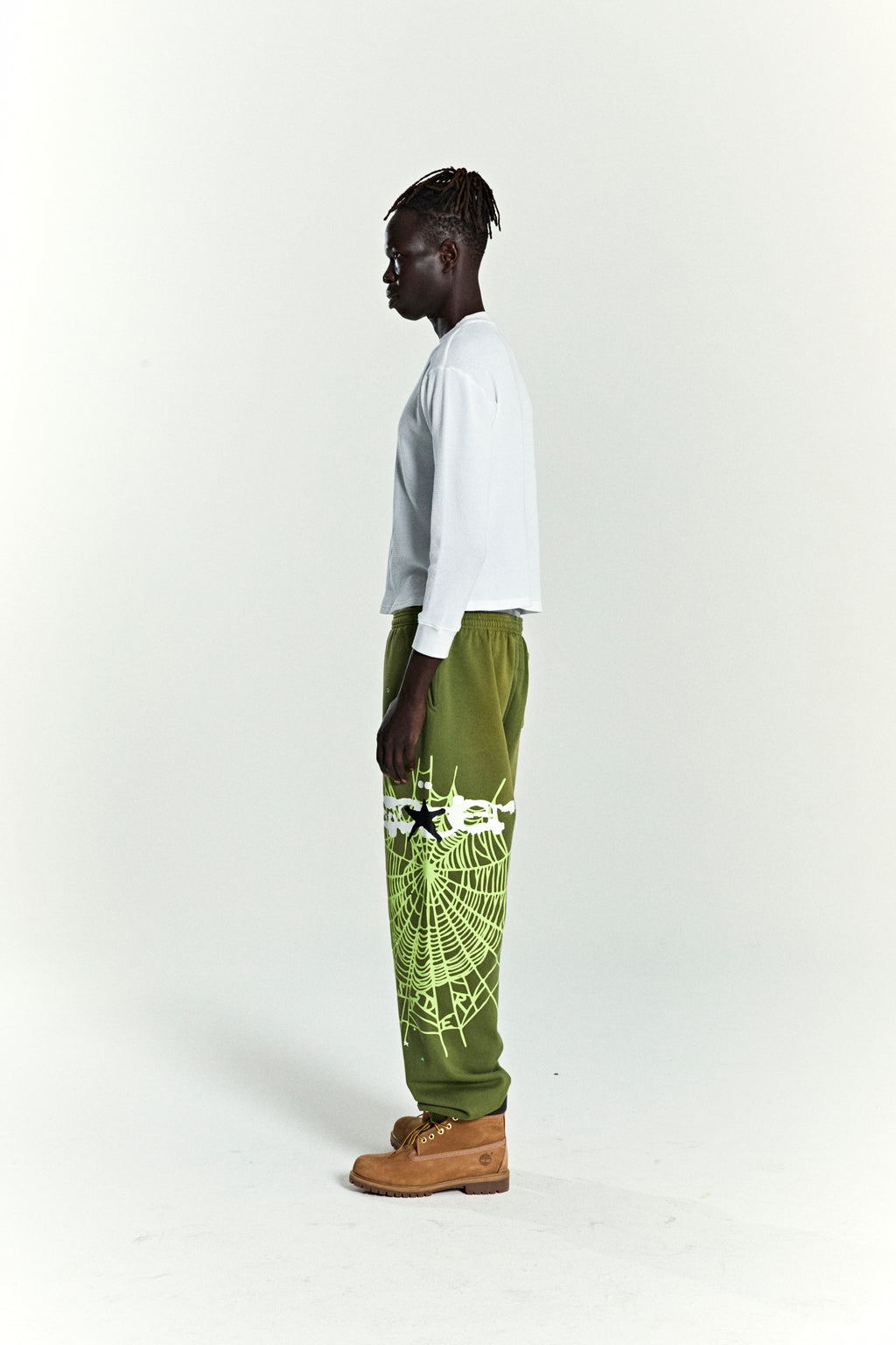 Olive green HEAVY WEB SWEATPANT with white SP5DER web graphic and scattered stars, worn by a model.