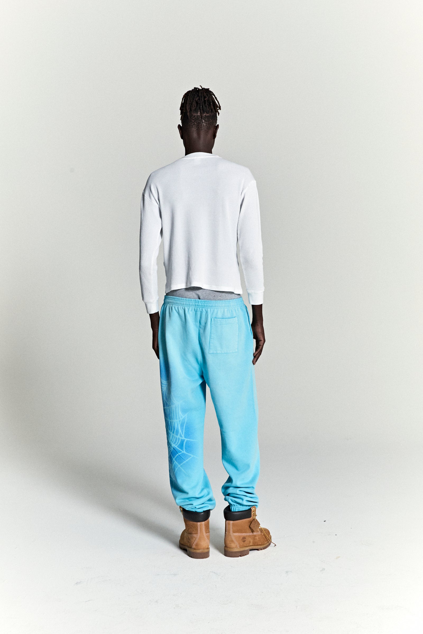 Model from behind wearing OG WEB V2 SPRAY SWEATPANT in light blue cotton fleece with spray web design.
