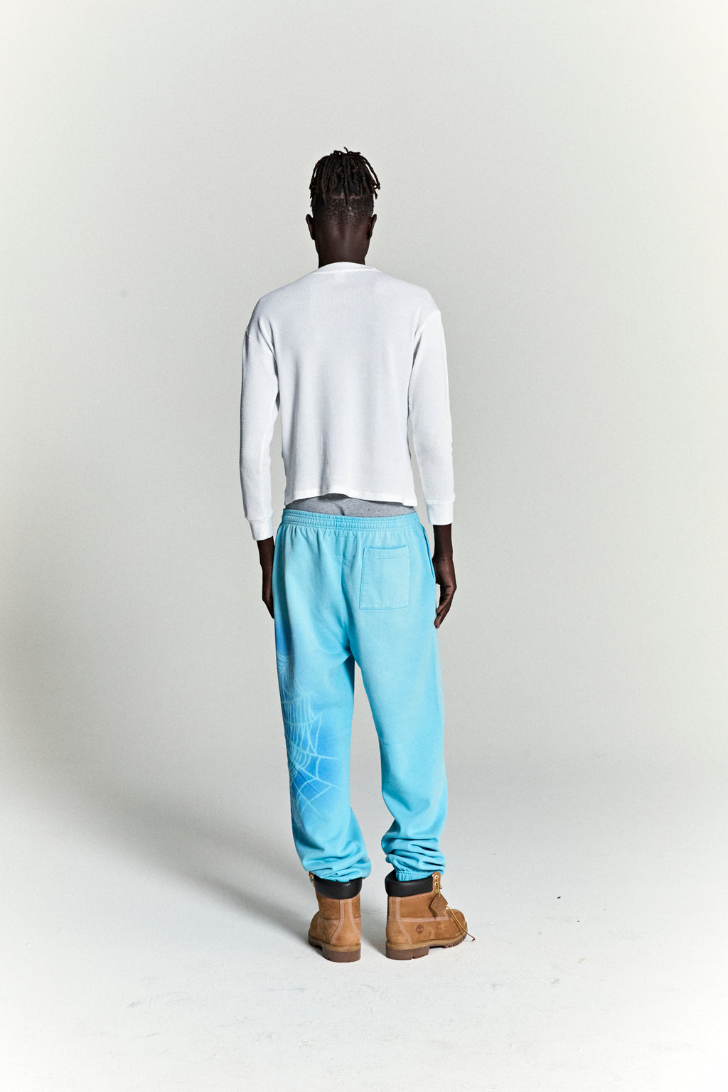 Model from behind wearing OG WEB V2 SPRAY SWEATPANT in light blue cotton fleece with spray web design.