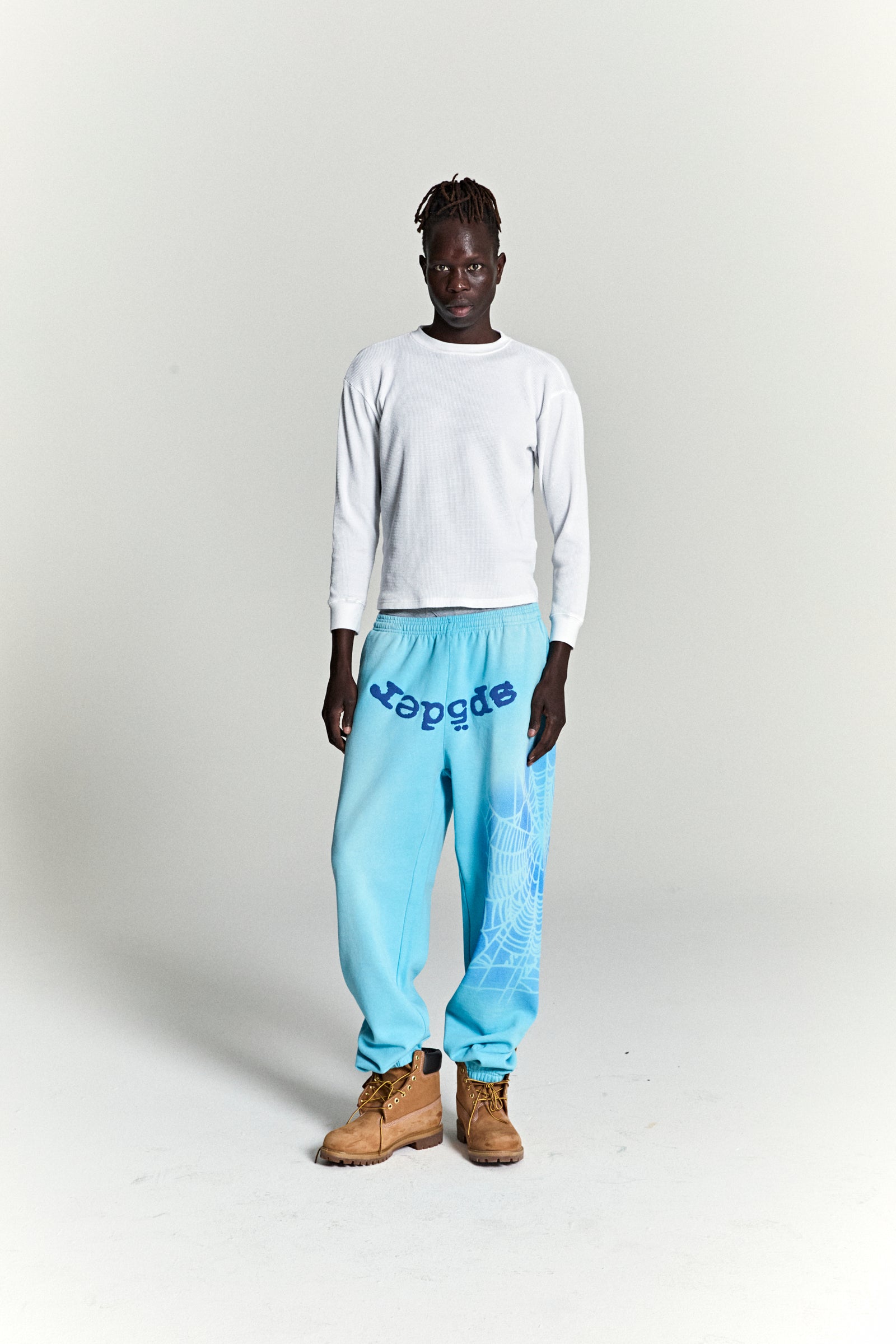 Model wearing OG WEB V2 SPRAY SWEATPANT in light blue, featuring "SP5DER" text and spray web design.
