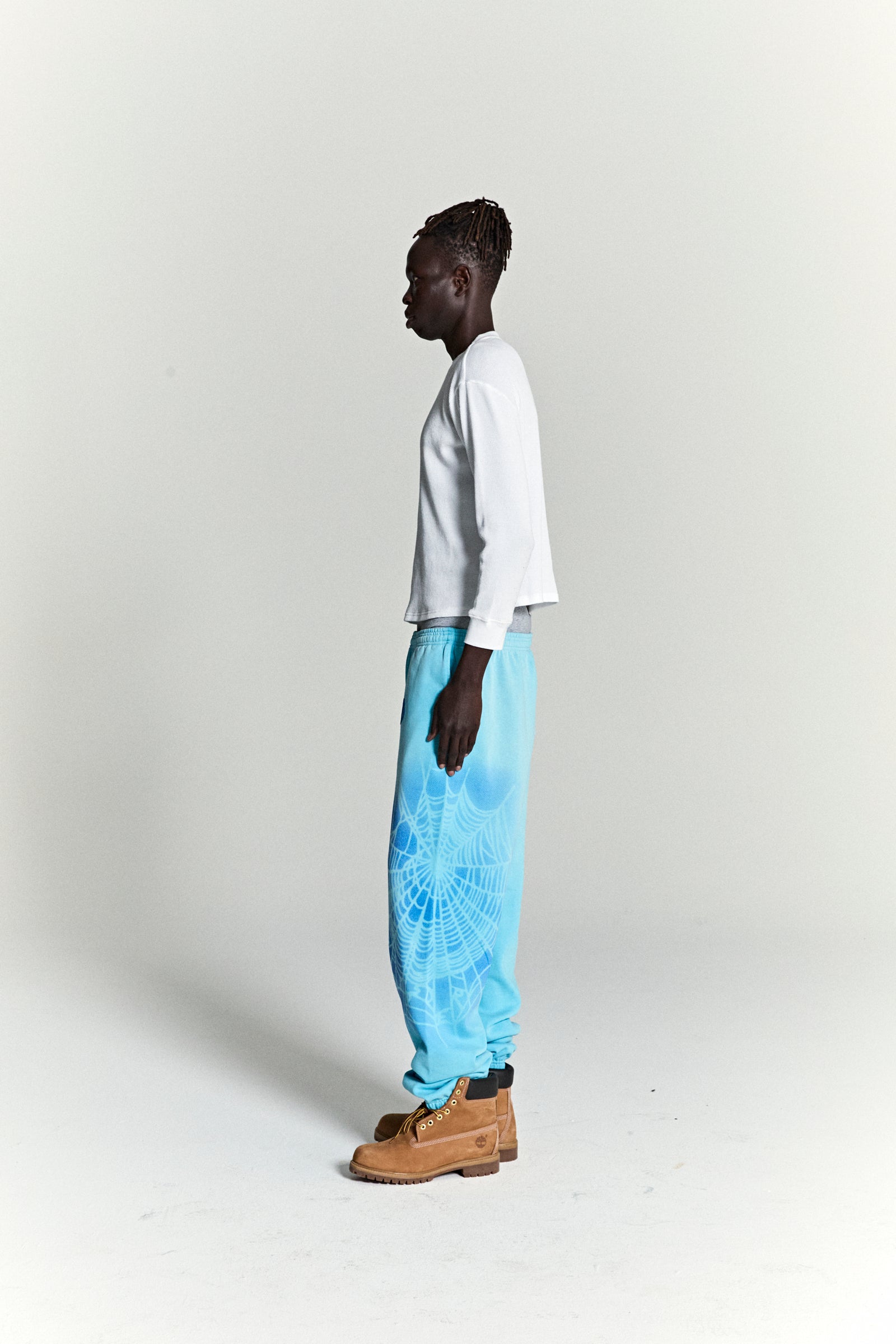 Model wearing OG WEB V2 SPRAY SWEATPANT, light blue 100% cotton fleece with white spray web design.