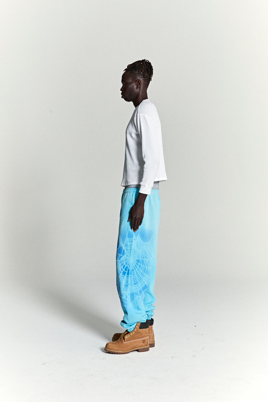 Model wearing OG WEB V2 SPRAY SWEATPANT, light blue 100% cotton fleece with white spray web design.