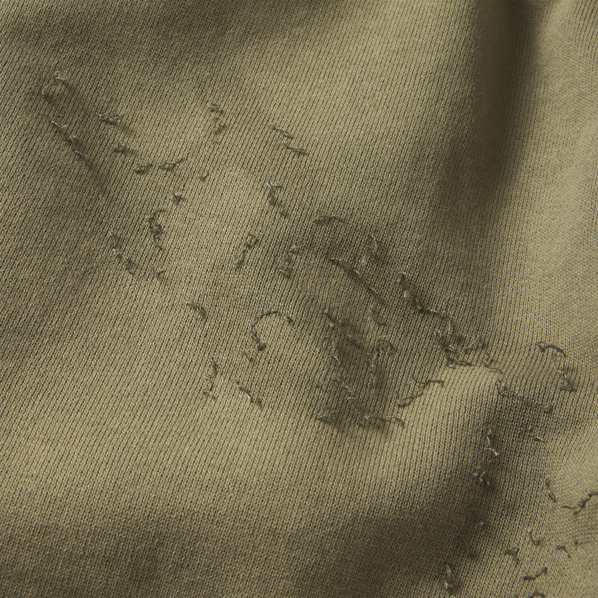 Close-up of olive green cotton fleece sweatpants featuring distressed SP5DER graphic print and stitching details.