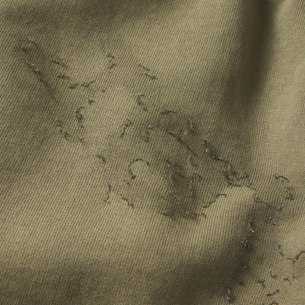 Close-up of olive green cotton fleece sweatpants featuring distressed SP5DER graphic print and stitching details.