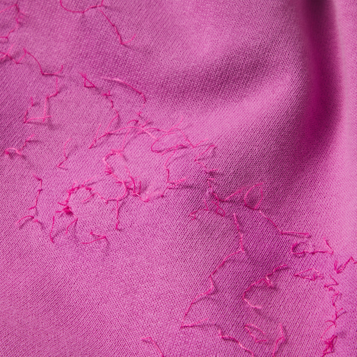 Close-up of pink 100% cotton fleece sweatpants featuring distressed SP5DER graphic print and thread detailing.