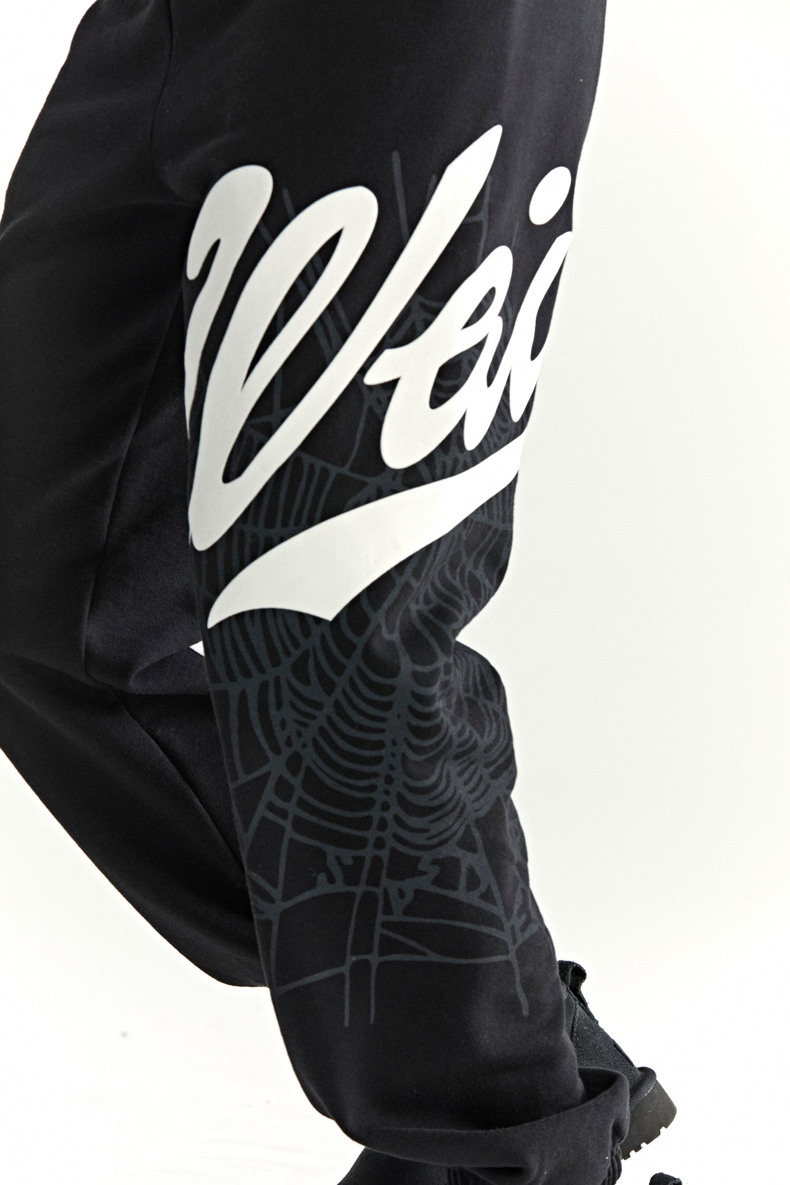 Black cotton fleece sweatpants with white "Wait" script and grey spiderweb print on side leg.