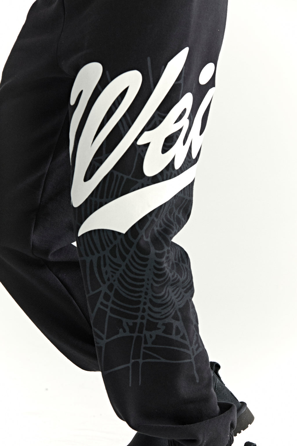 Black cotton fleece sweatpants with white "Wait" script and grey spiderweb print on side leg.