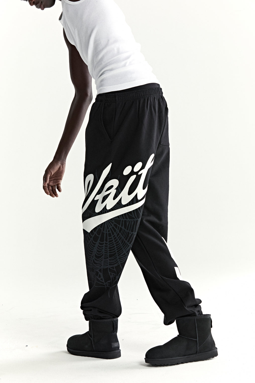 Black cotton fleece sweatpants with "Wait" script, web print, and elastic cuffs.