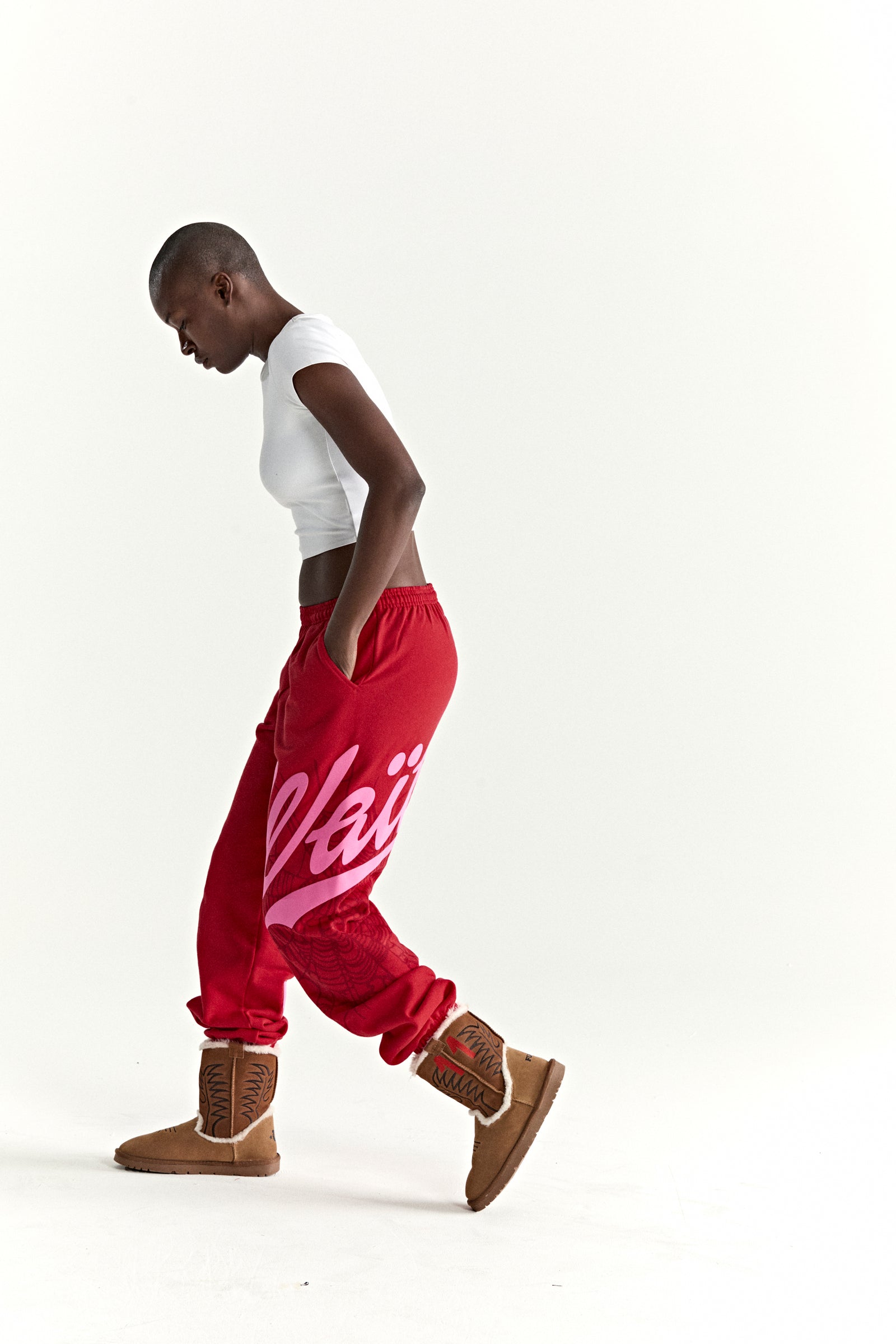 Red cotton fleece sweatpants with pink 'Wait' script and web print, worn by a model.
