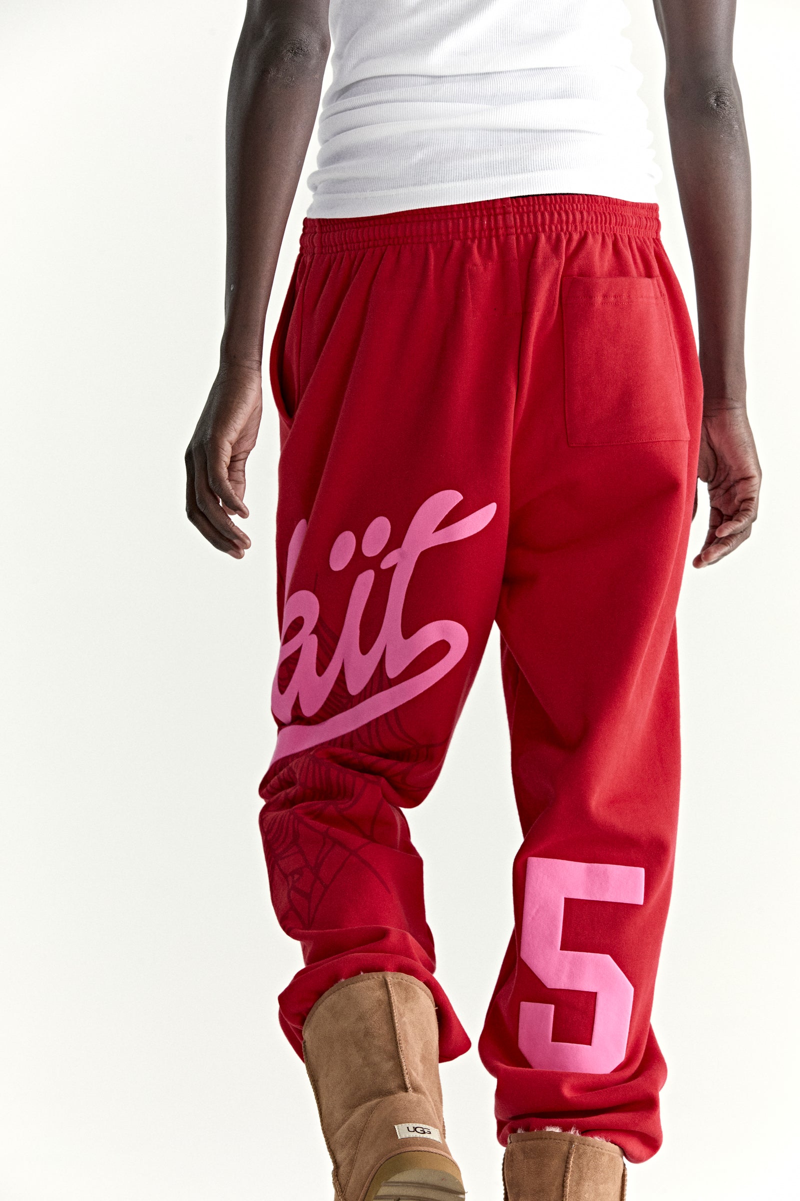 Red cotton fleece sweatpants with pink "Wait" script, web print, and "5" motif.