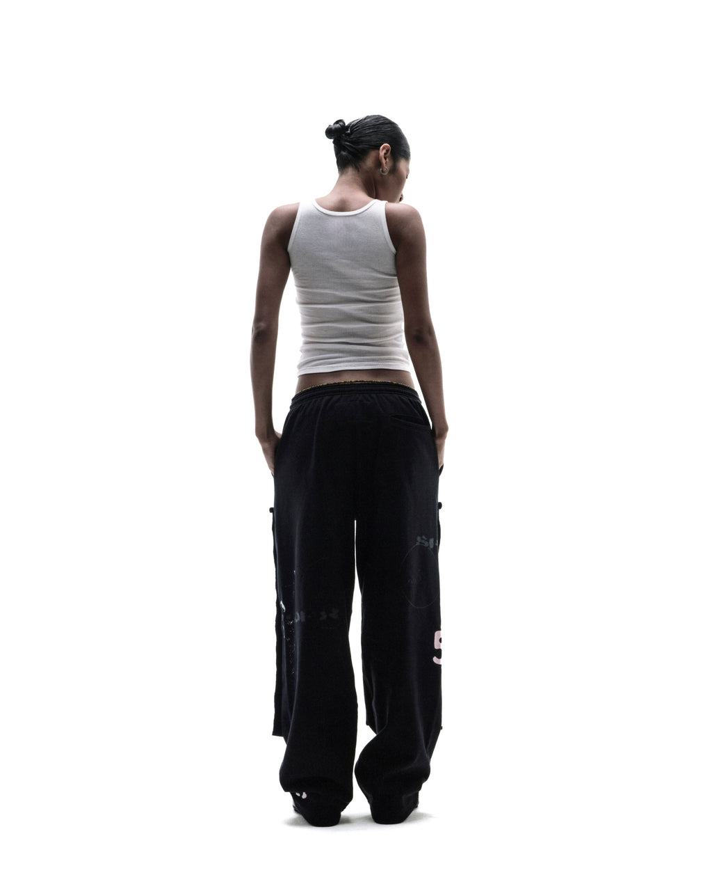 A model seen from behind wearing a white ribbed tank top and oversized black cargo pants against a white background.