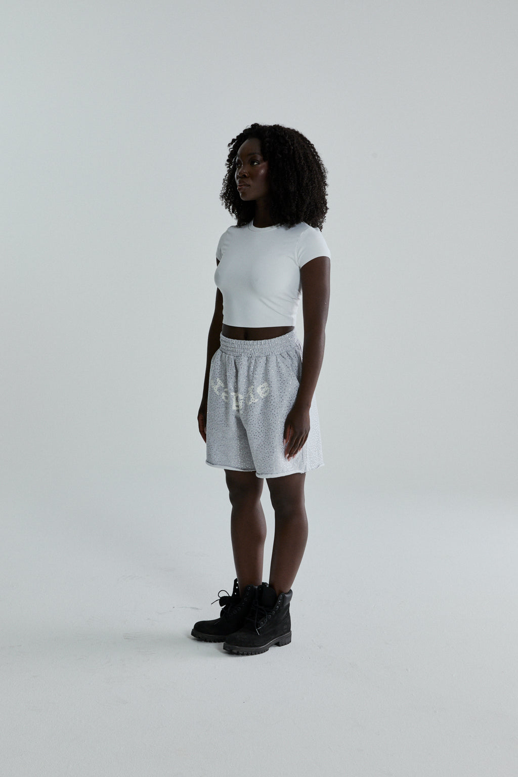Woman wearing gray VVS SWEATSHORT with tonal rhinestones, SP5DER text, and raw hem.