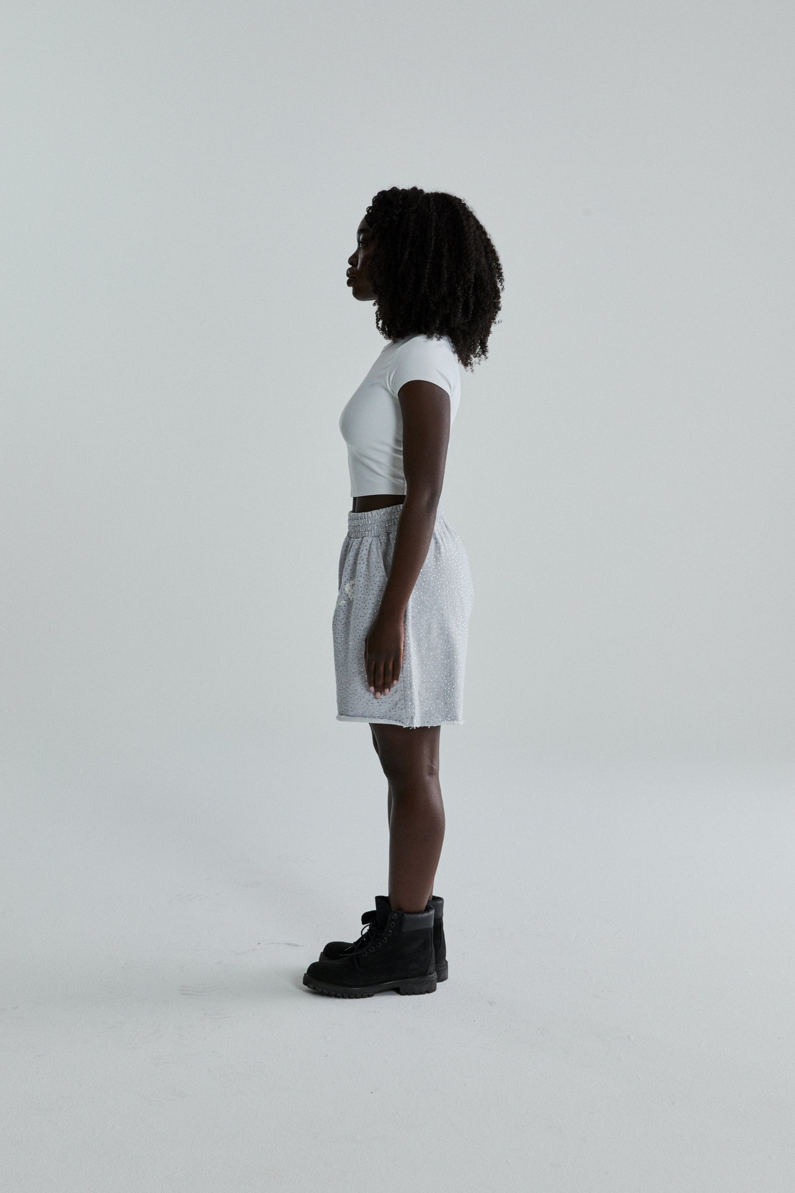 Woman wearing VVS SWEATSHORT: light grey 13oz cotton fleece shorts with tonal rhinestones, SP5DER text, and raw hem.
