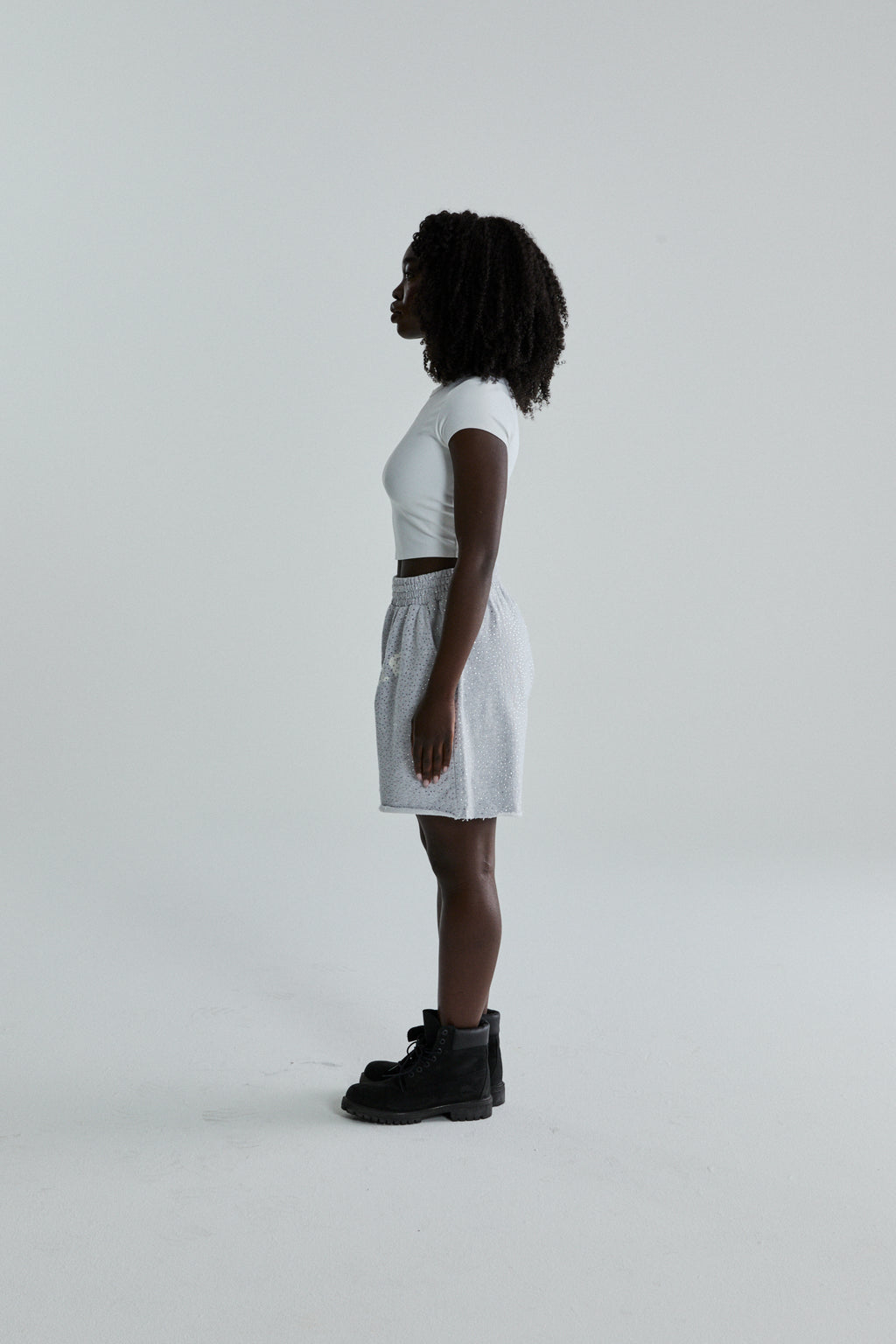 Woman wearing VVS SWEATSHORT: light grey 13oz cotton fleece shorts with tonal rhinestones, SP5DER text, and raw hem.