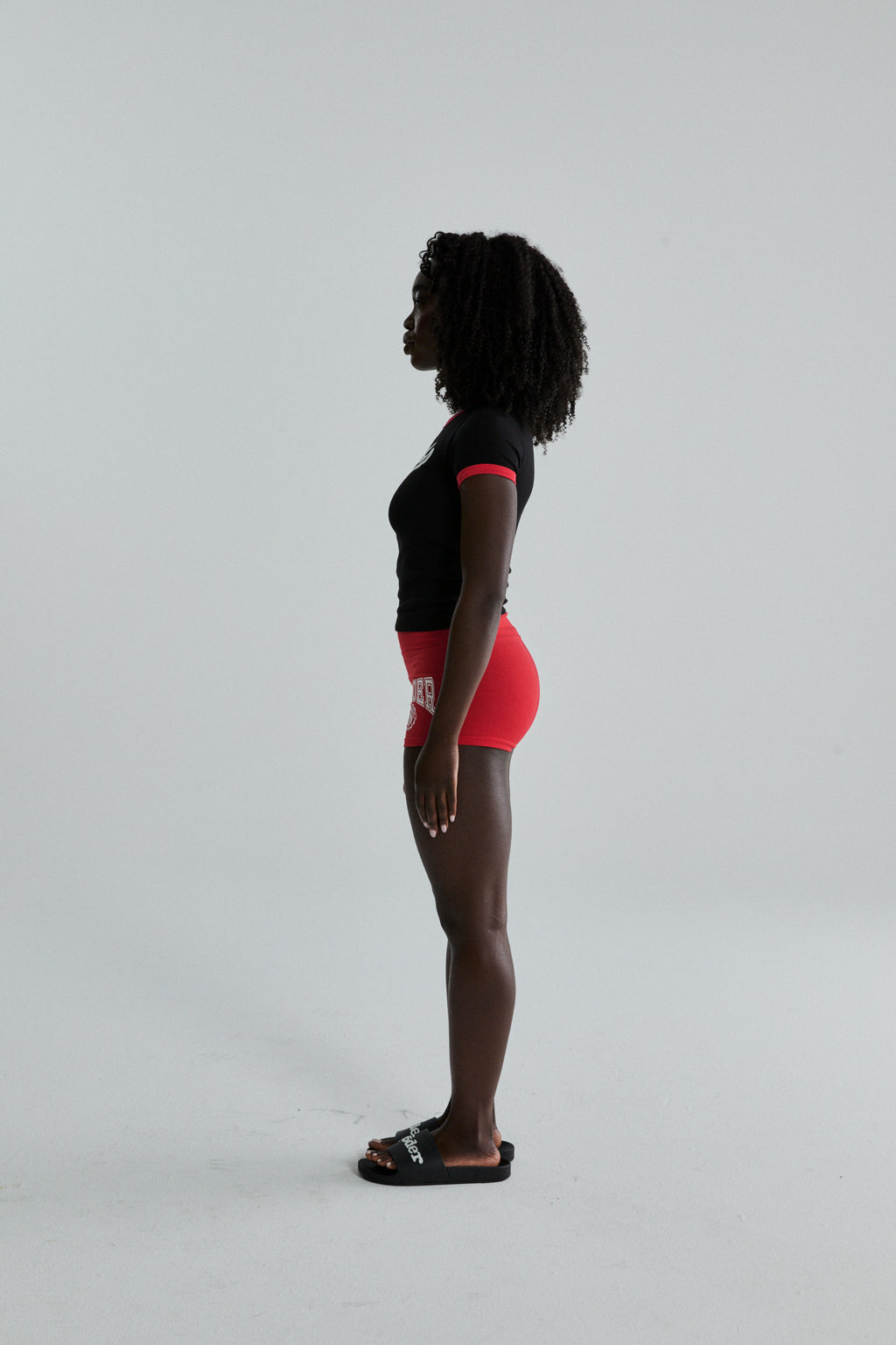 Black cotton/spandex cropped tee with red trim, paired with red shorts, on a woman in profile.