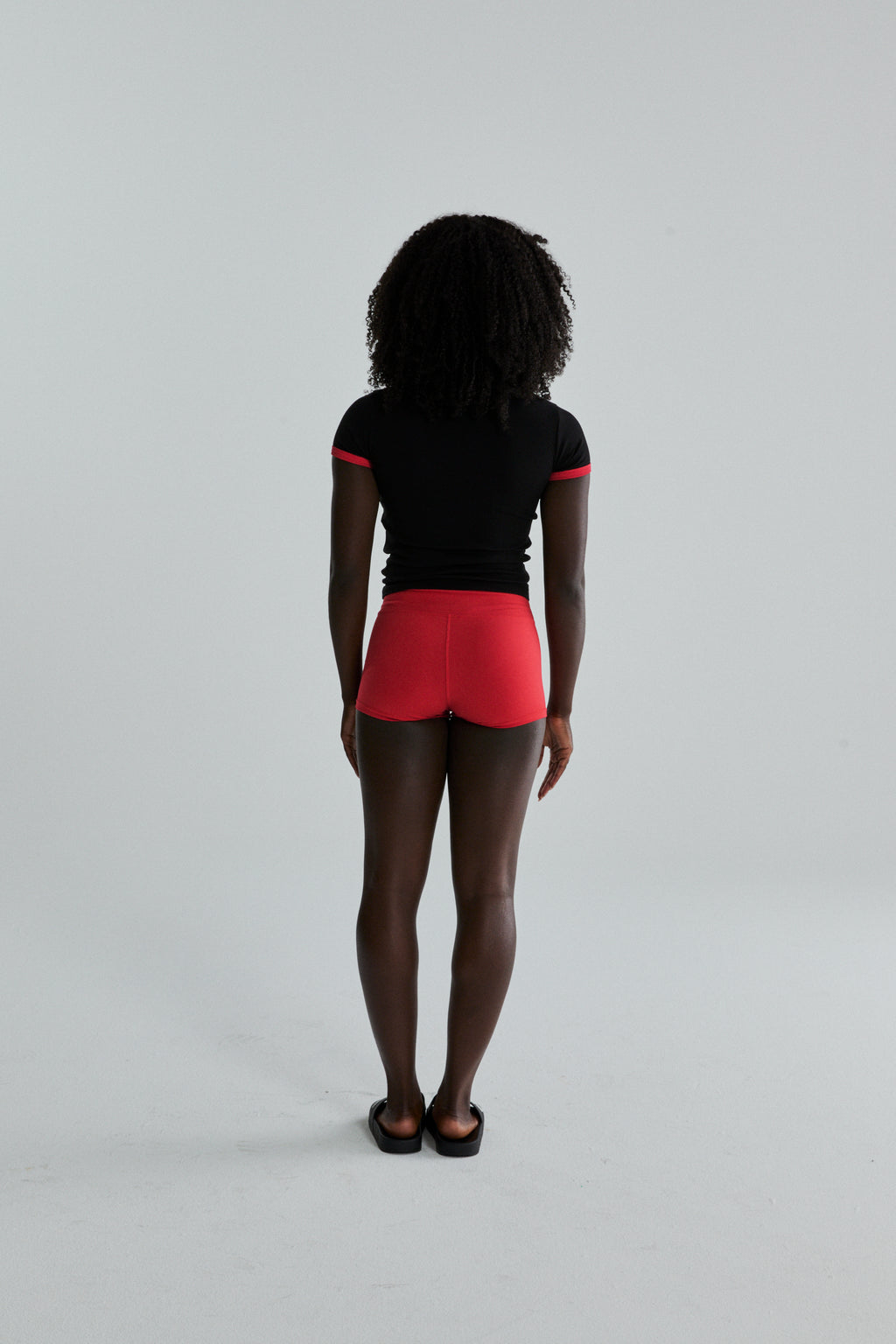 Back view of model in black cropped tee with red trim and red fitted shorts.