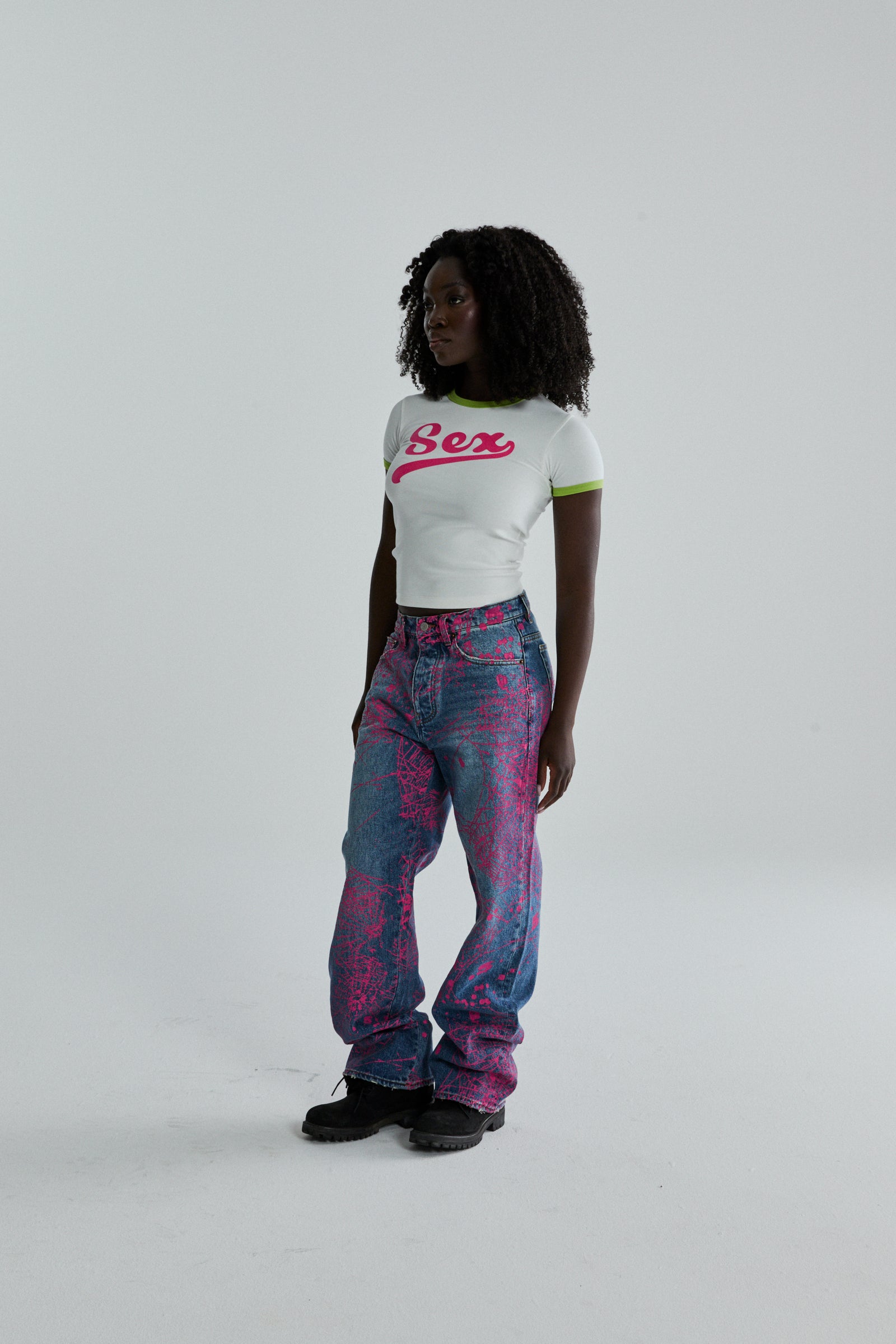 Woman in white cropped "Sex" baby tee with green trim and pink graphic print jeans.