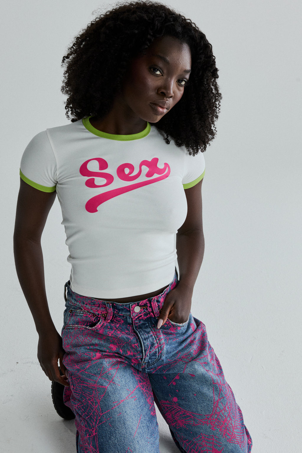 White cotton/spandex cropped tee with "Sex" graphic, green ribbed trim, worn by a model.