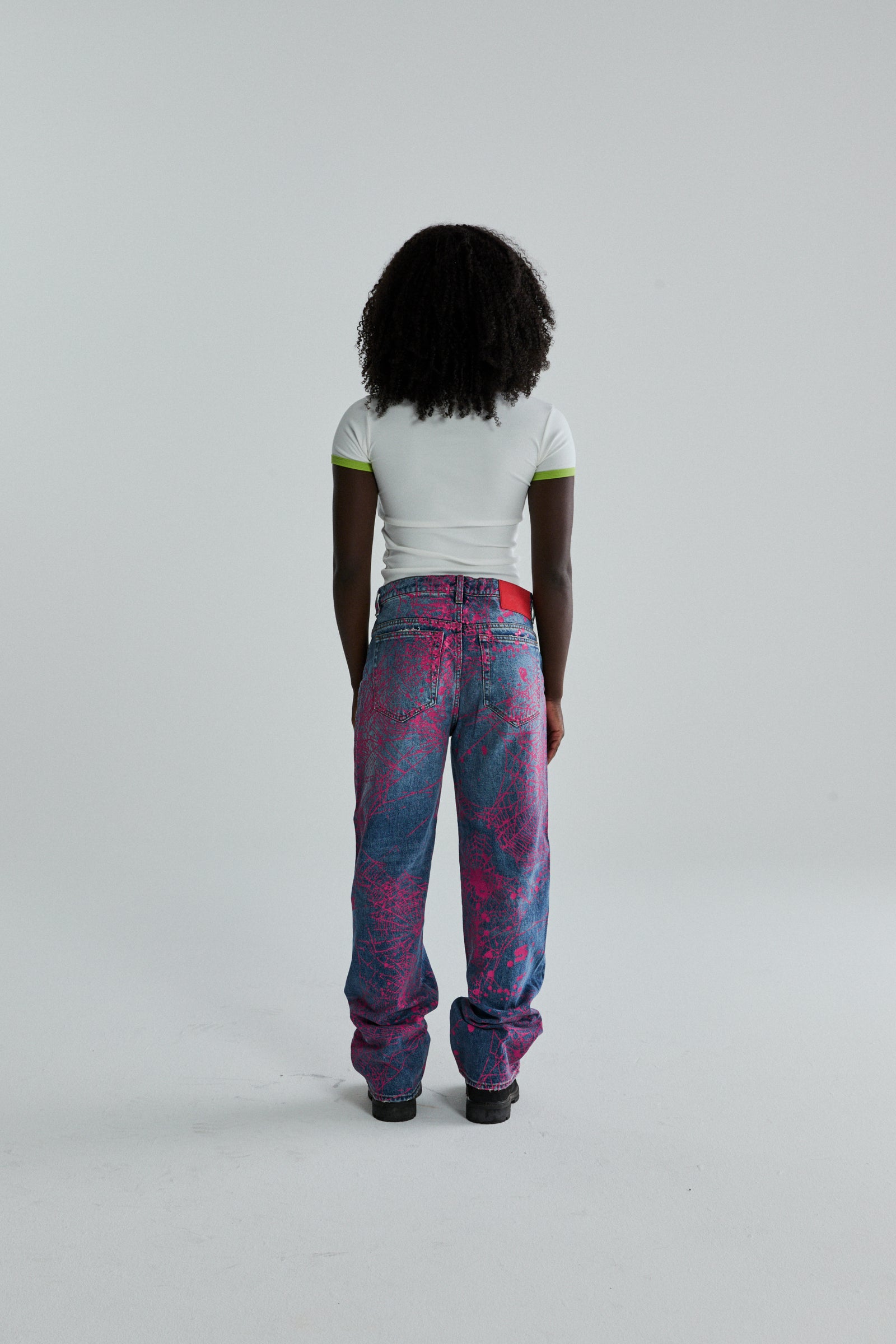 Woman from behind wearing a white cropped tee with green trim and baggy pink and blue graphic print jeans.