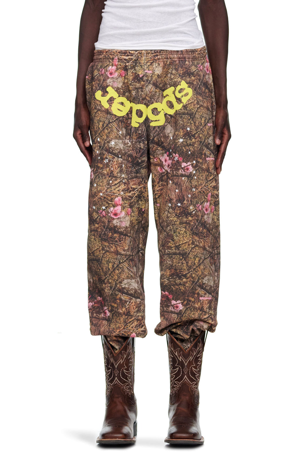 Real Tree OG Web Sweatpant: Brown camo fleece with pink flowers, yellow "sp5der" text, worn with cowboy boots.