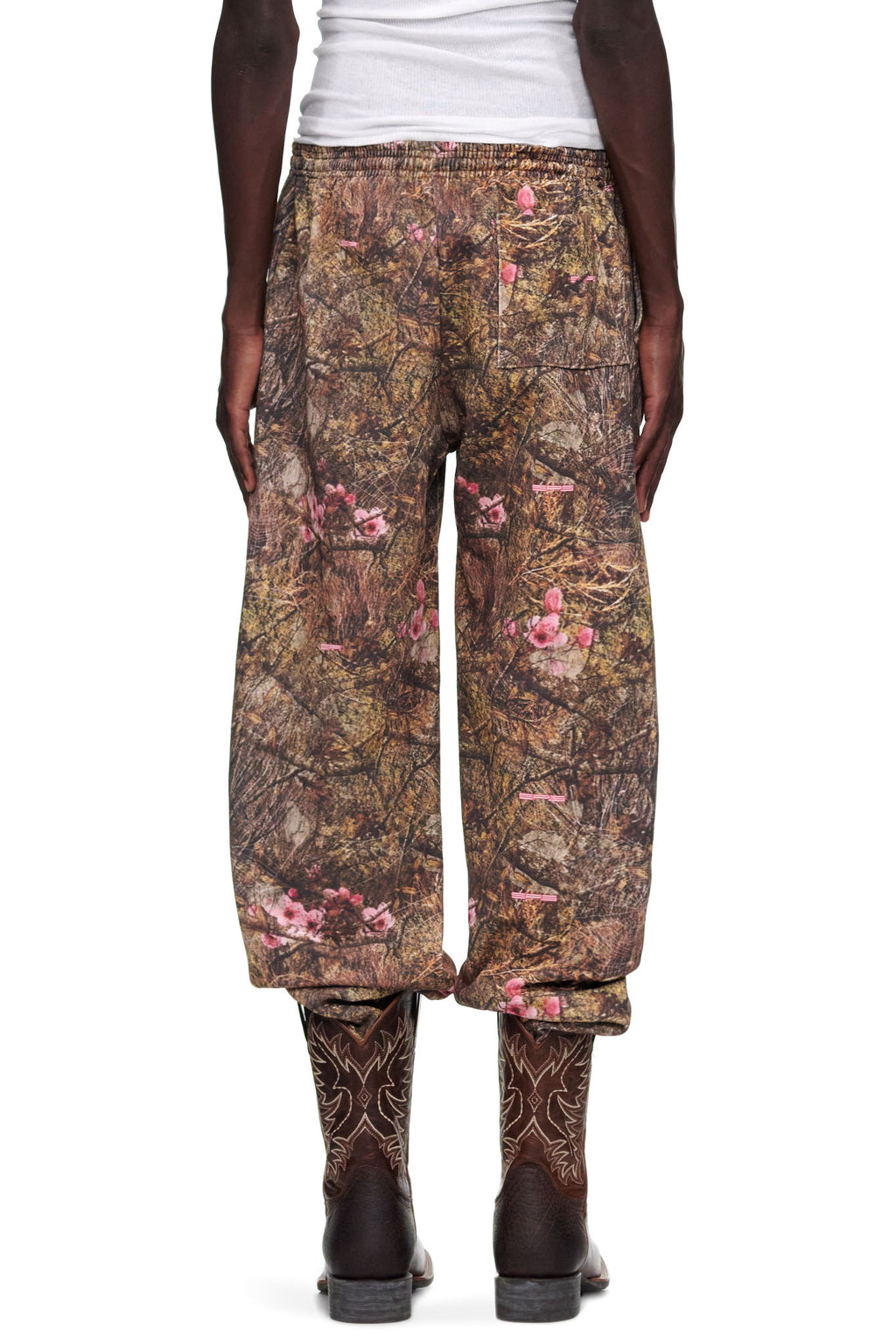 Male model in REAL TREE OG WEB SWEATPANT, brown camo with pink puff print, paired with cowboy boots.